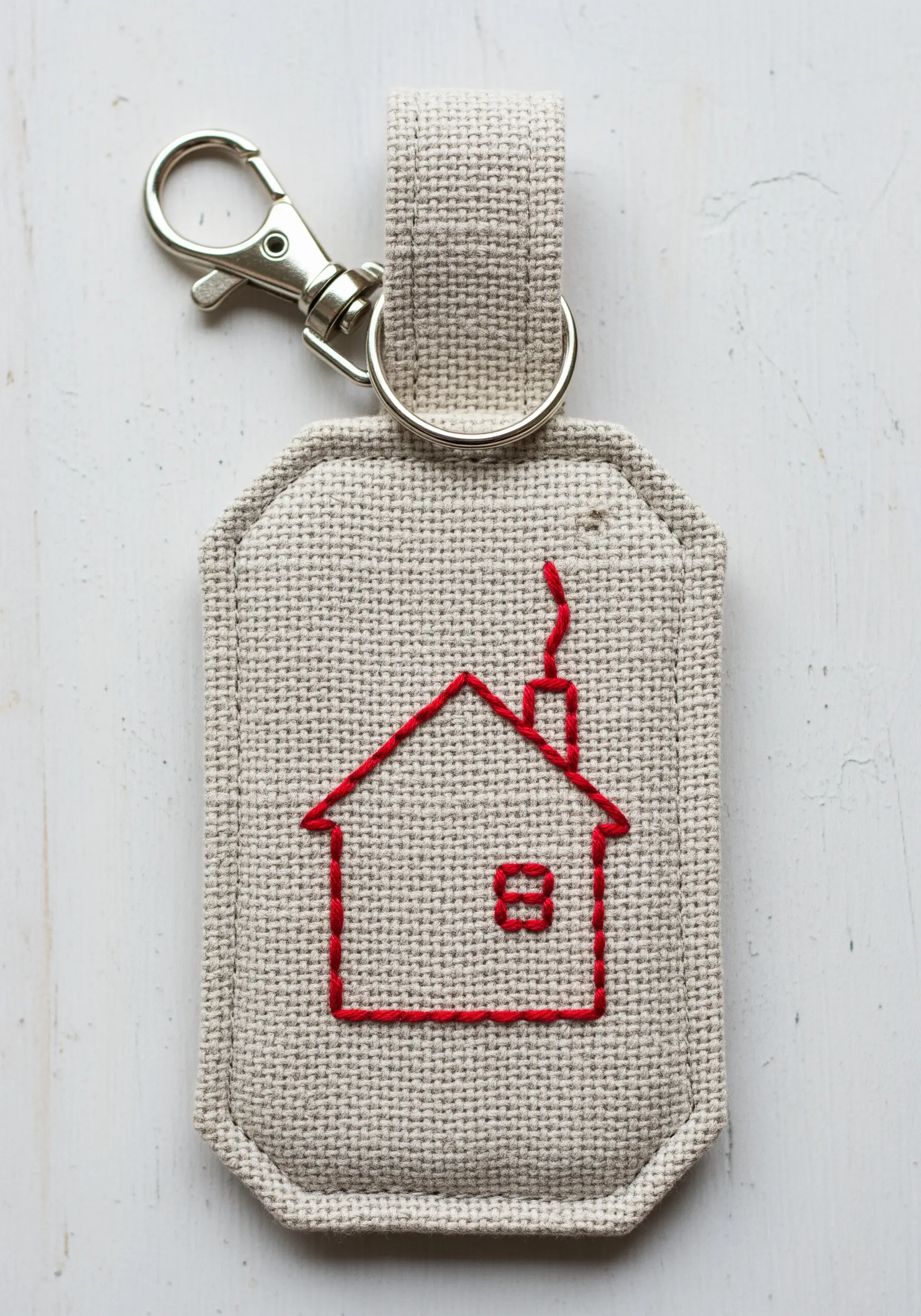 A simple red backstitch outline of a house on a fabric keychain fob.