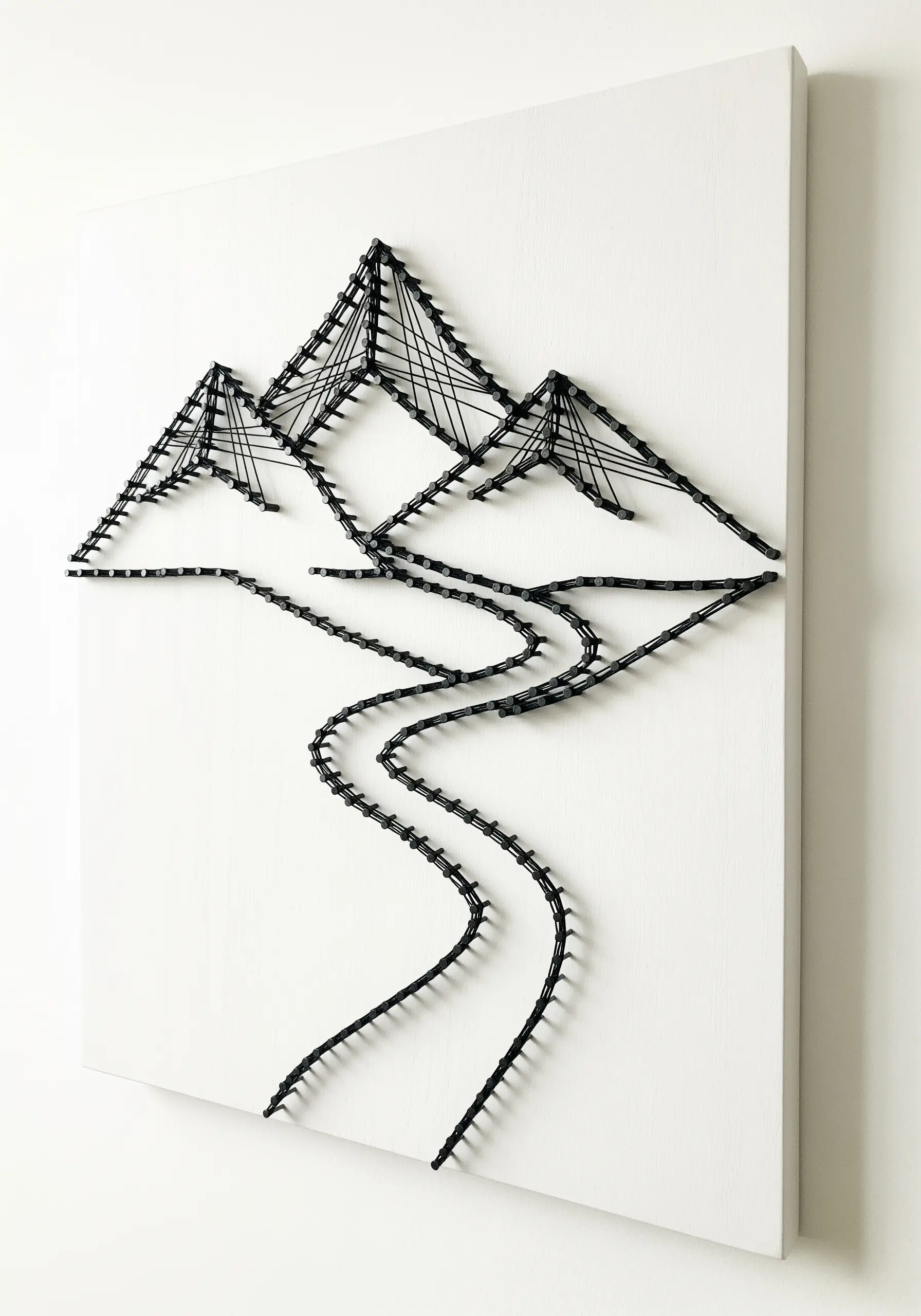 Minimalist black string art outline of mountains and a river on a white canvas.