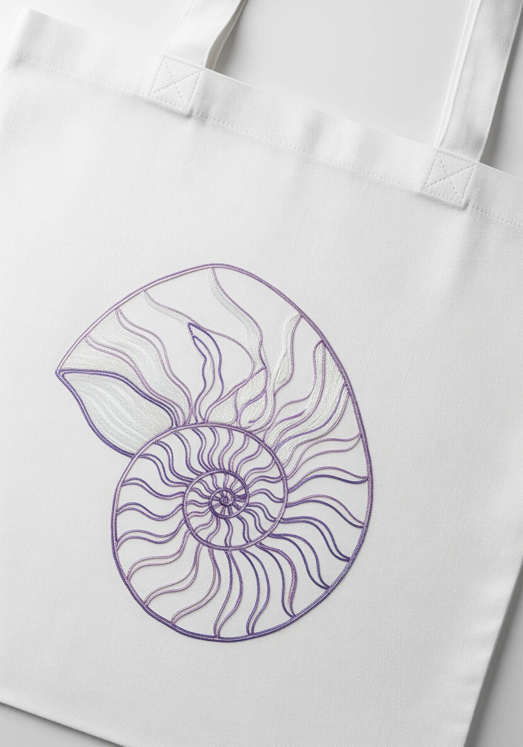 A fine line art embroidery of a nautilus shell in purple and white thread on a white tote.