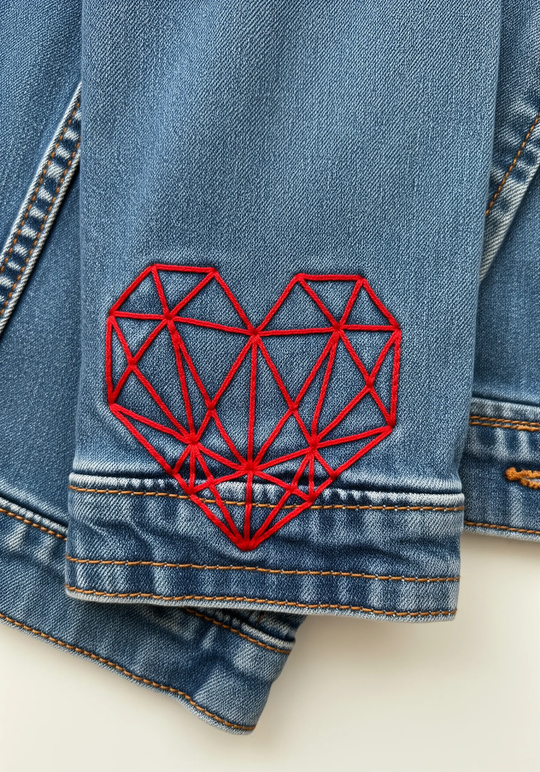 A red geometric heart made of intersecting straight lines embroidered on a denim jacket sleeve