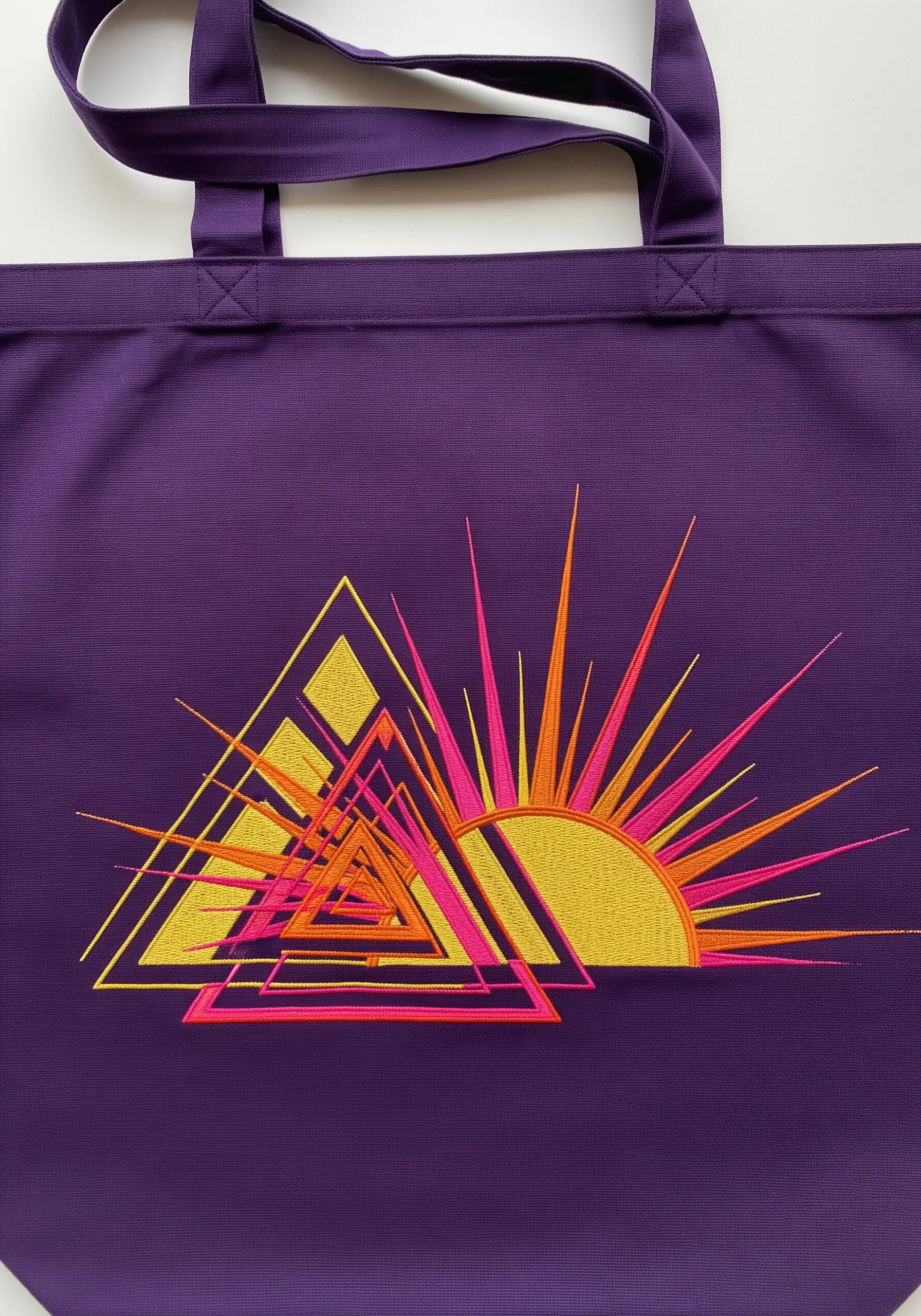 A geometric sunburst with sharp triangles embroidered in pink, orange, and yellow.