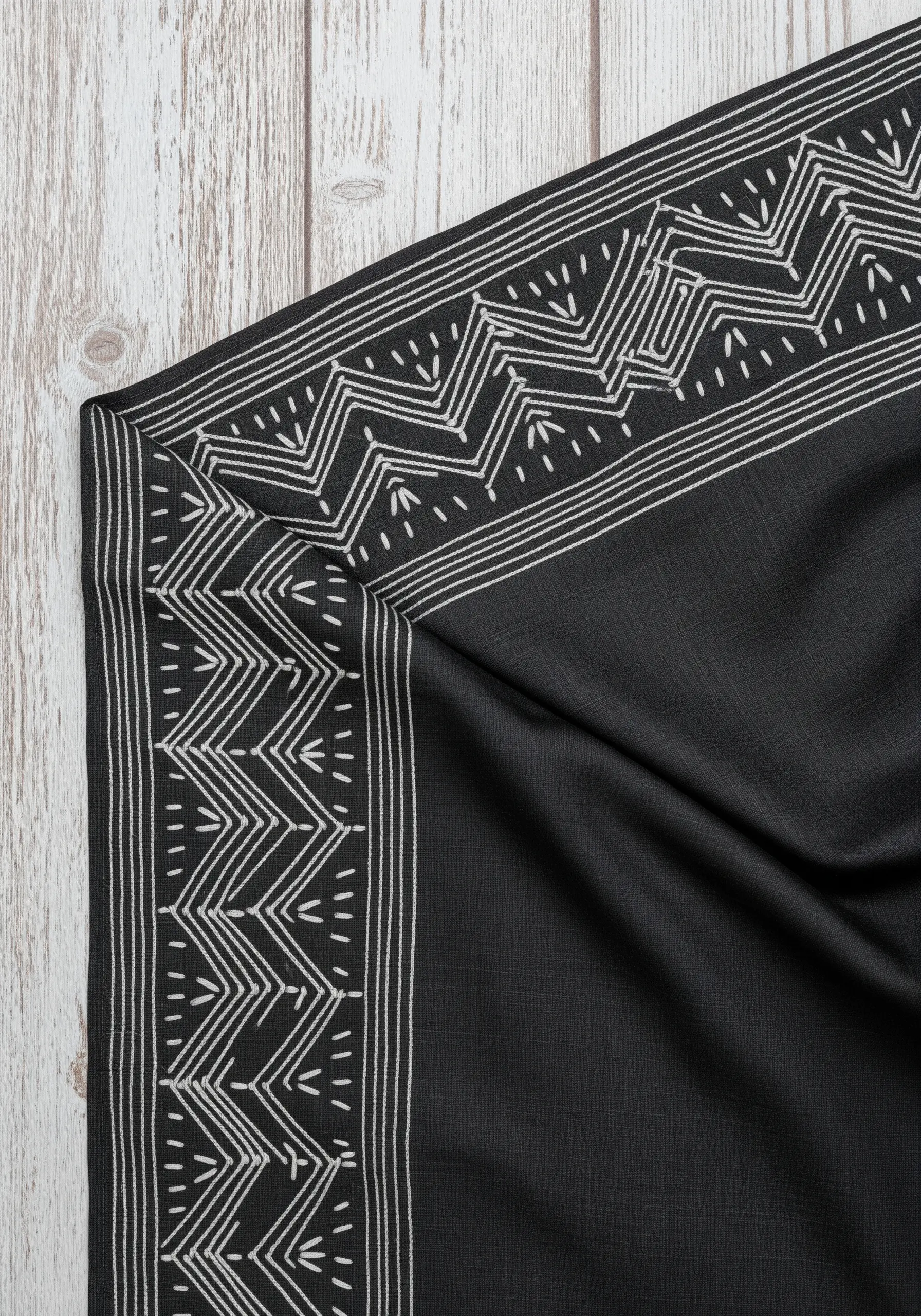 High-contrast white geometric embroidery border on black fabric.