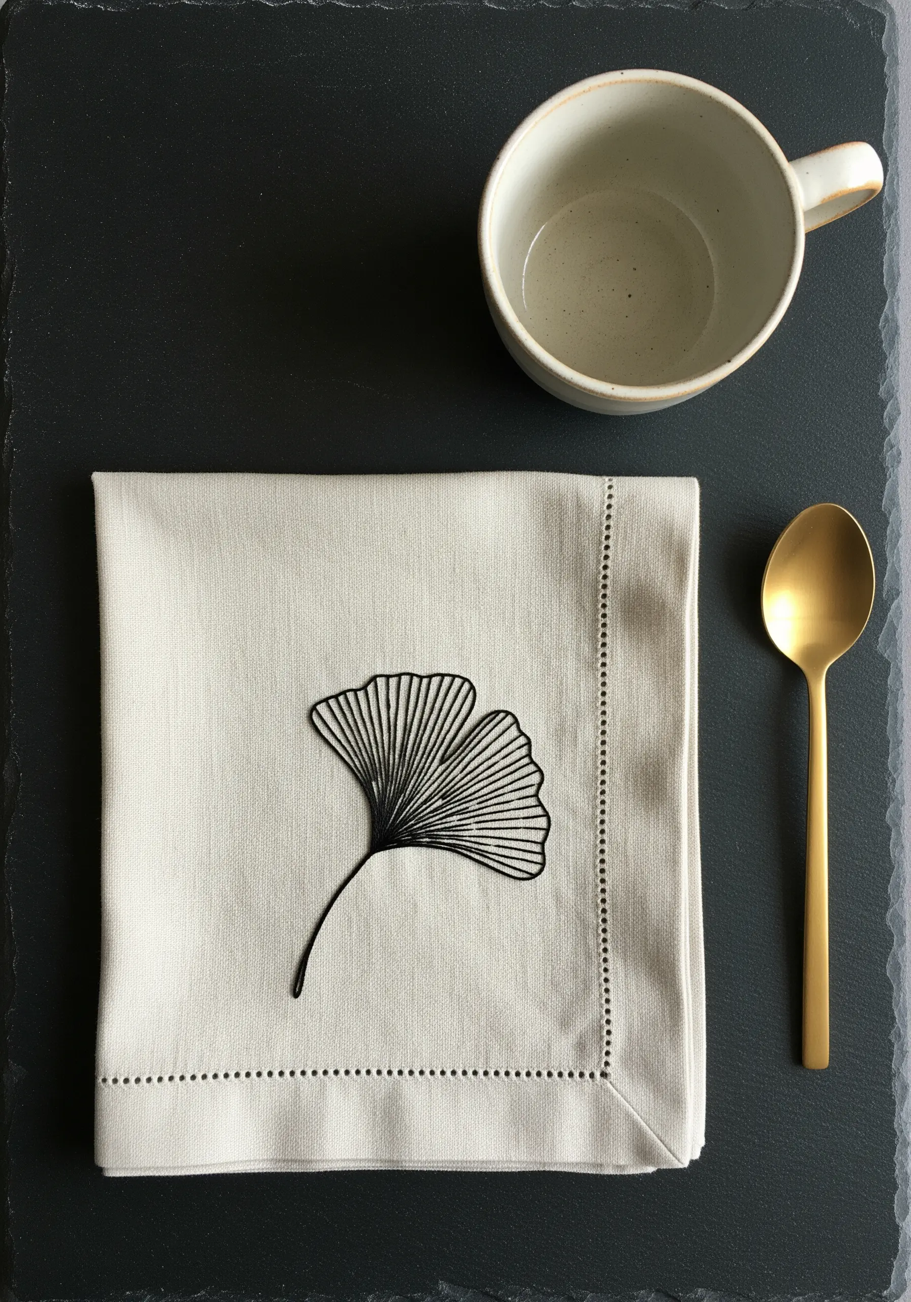 Minimalist black thread ginkgo leaf outline embroidered on a cream linen napkin.