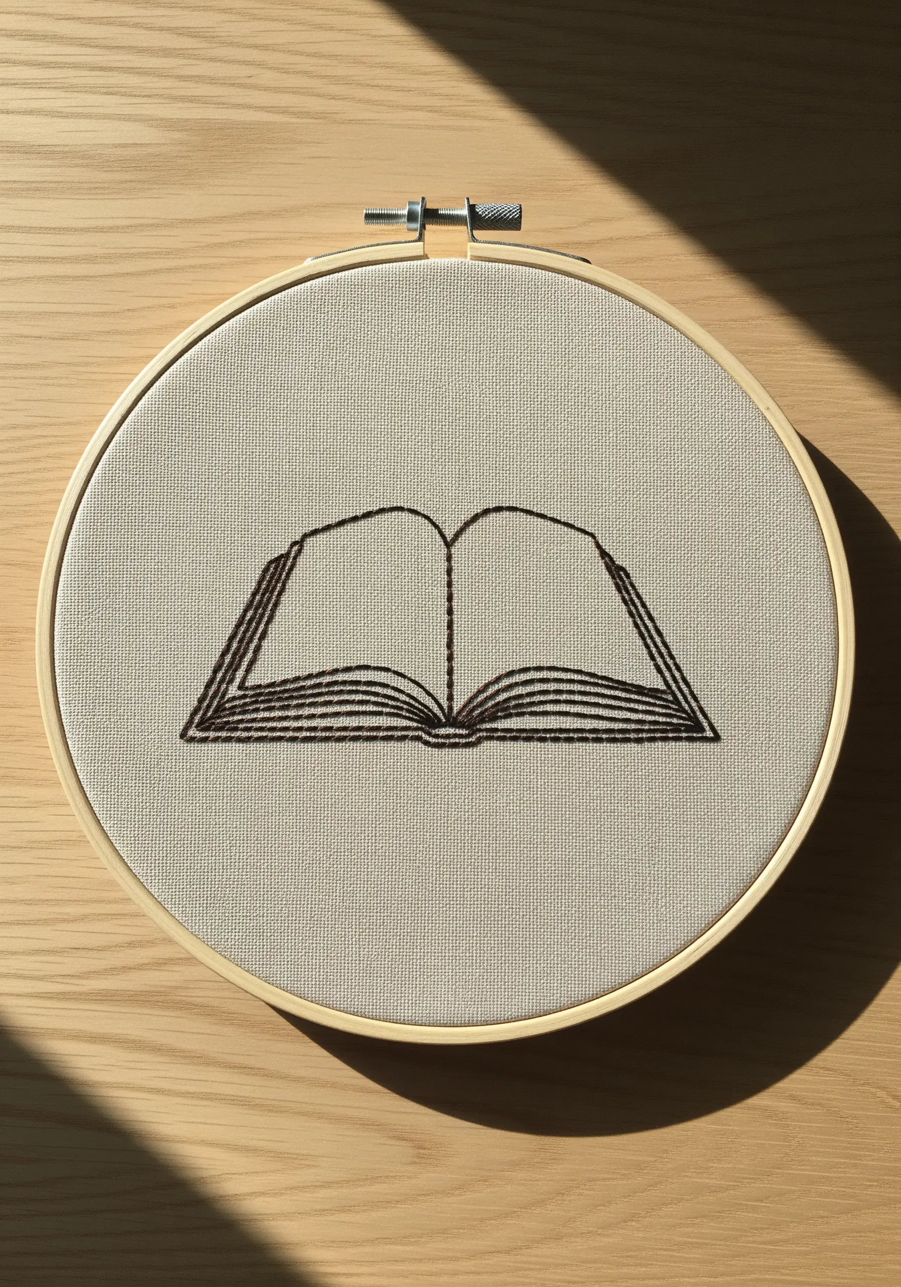An open book outline in dark brown thread on neutral fabric.