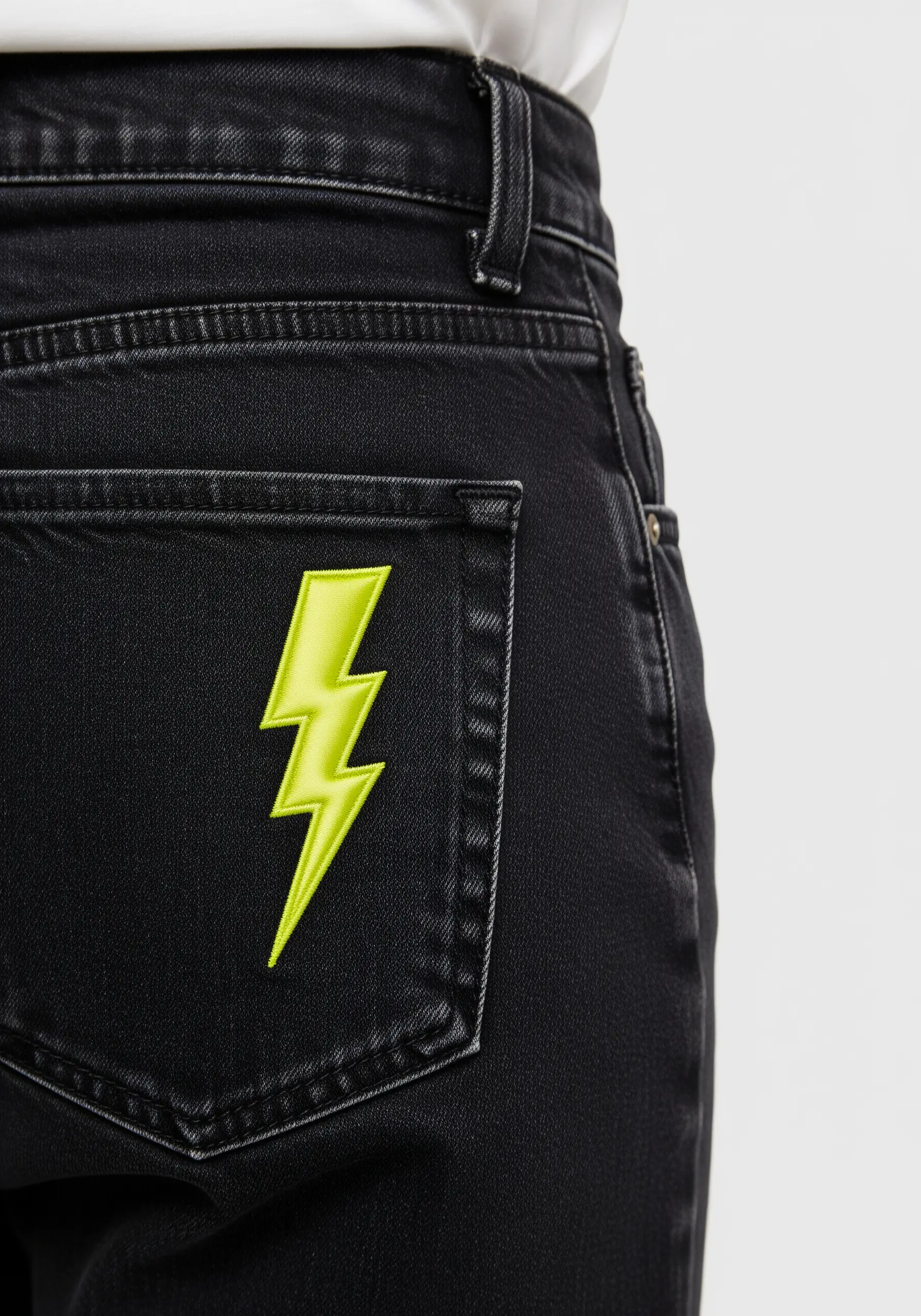 A bright neon yellow lightning bolt embroidered on the pocket of black jeans.
