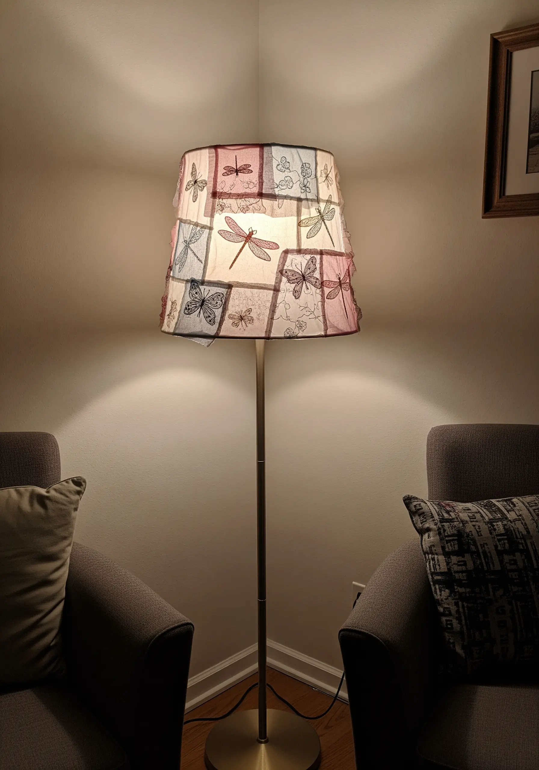 A patchwork lampshade made of sheer fabrics with embroidered dragonflies, lit from within.