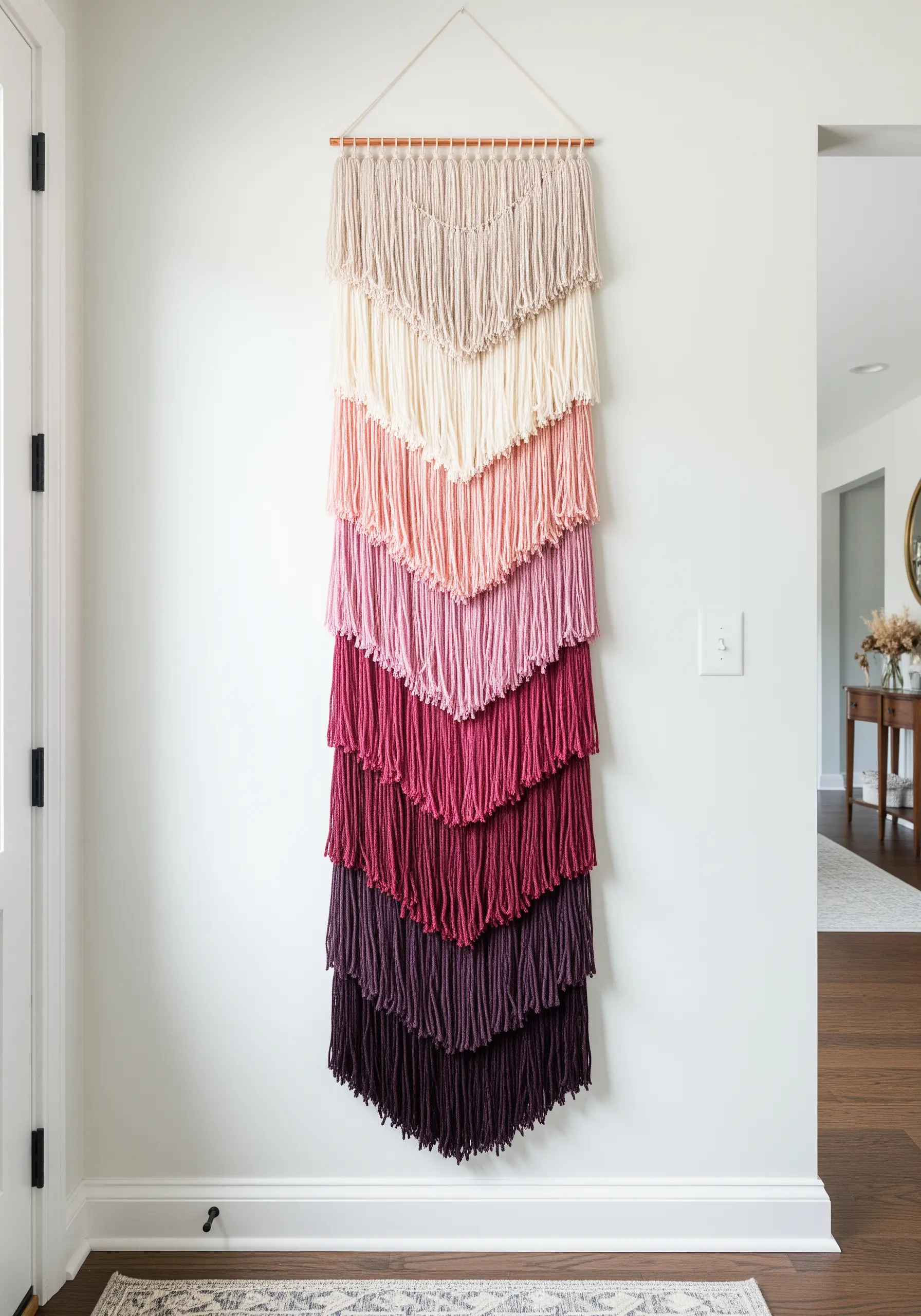 A long, tiered macrame wall hanging with a color gradient from light pink to deep burgundy.
