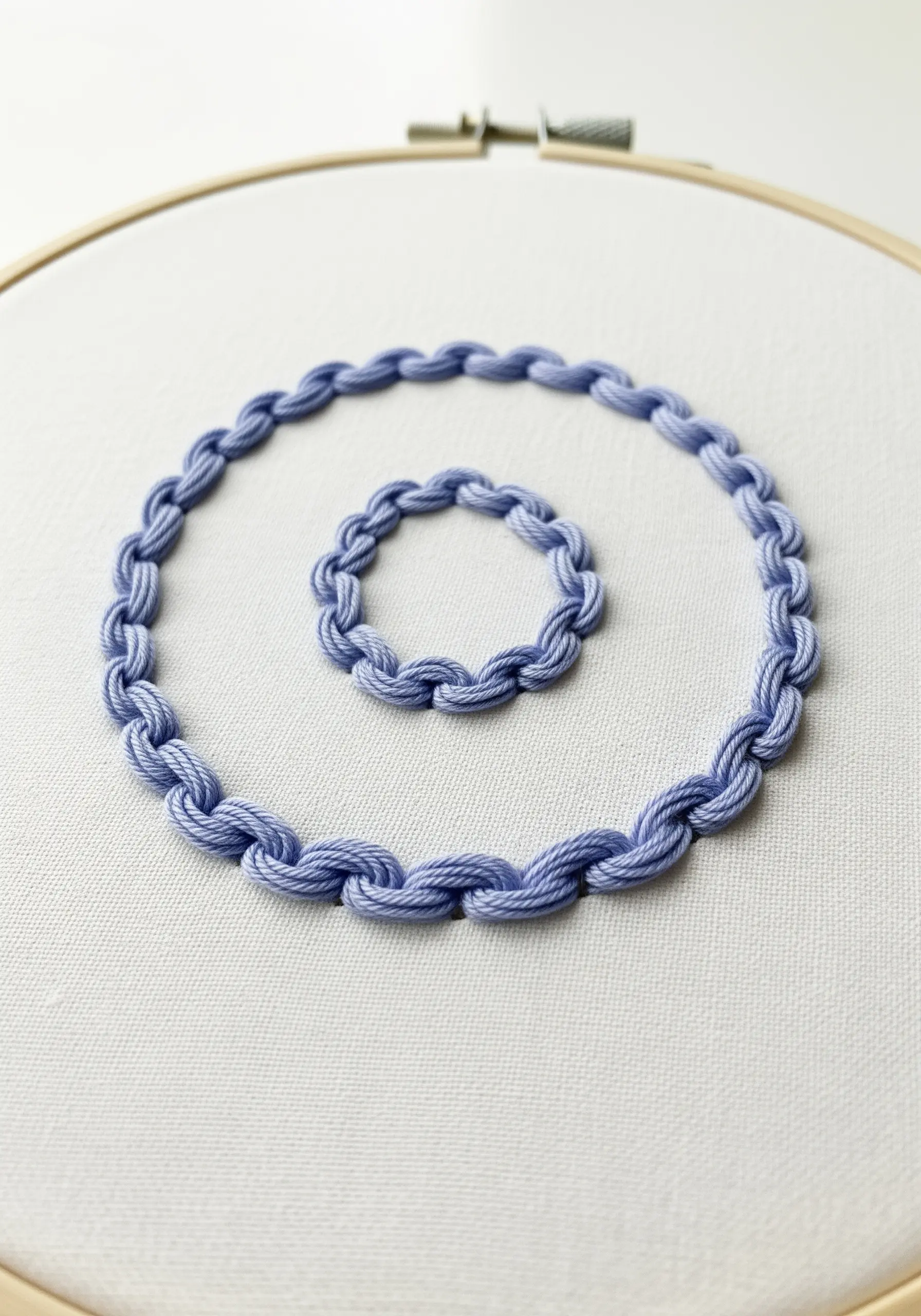 A spiral created with blue chain stitch on white fabric.