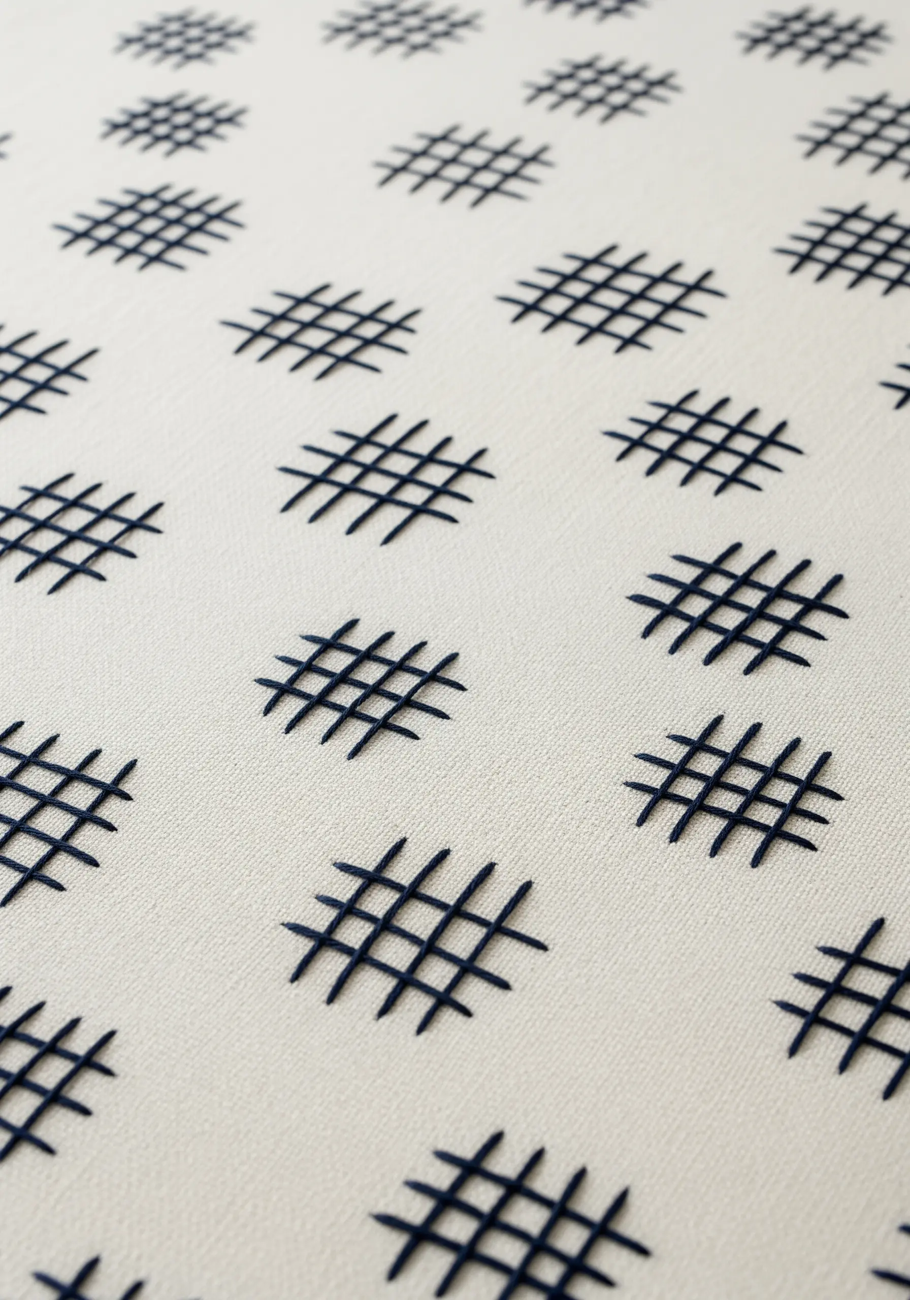 A repeating pattern of small, hand-stitched navy blue hash marks on a cream background.