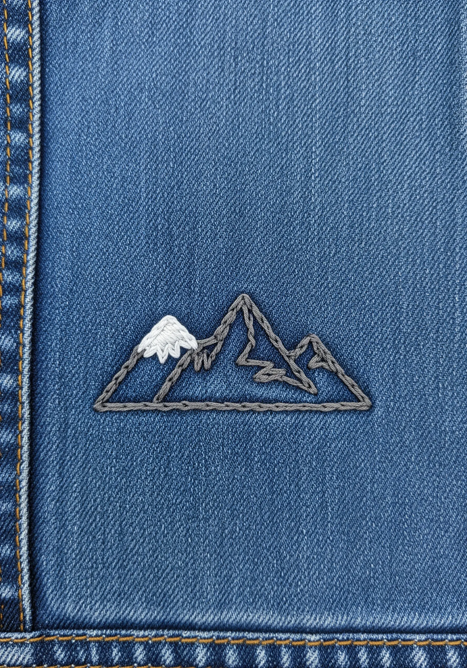 Minimalist line art embroidery of a mountain range with a snow-capped peak on blue denim