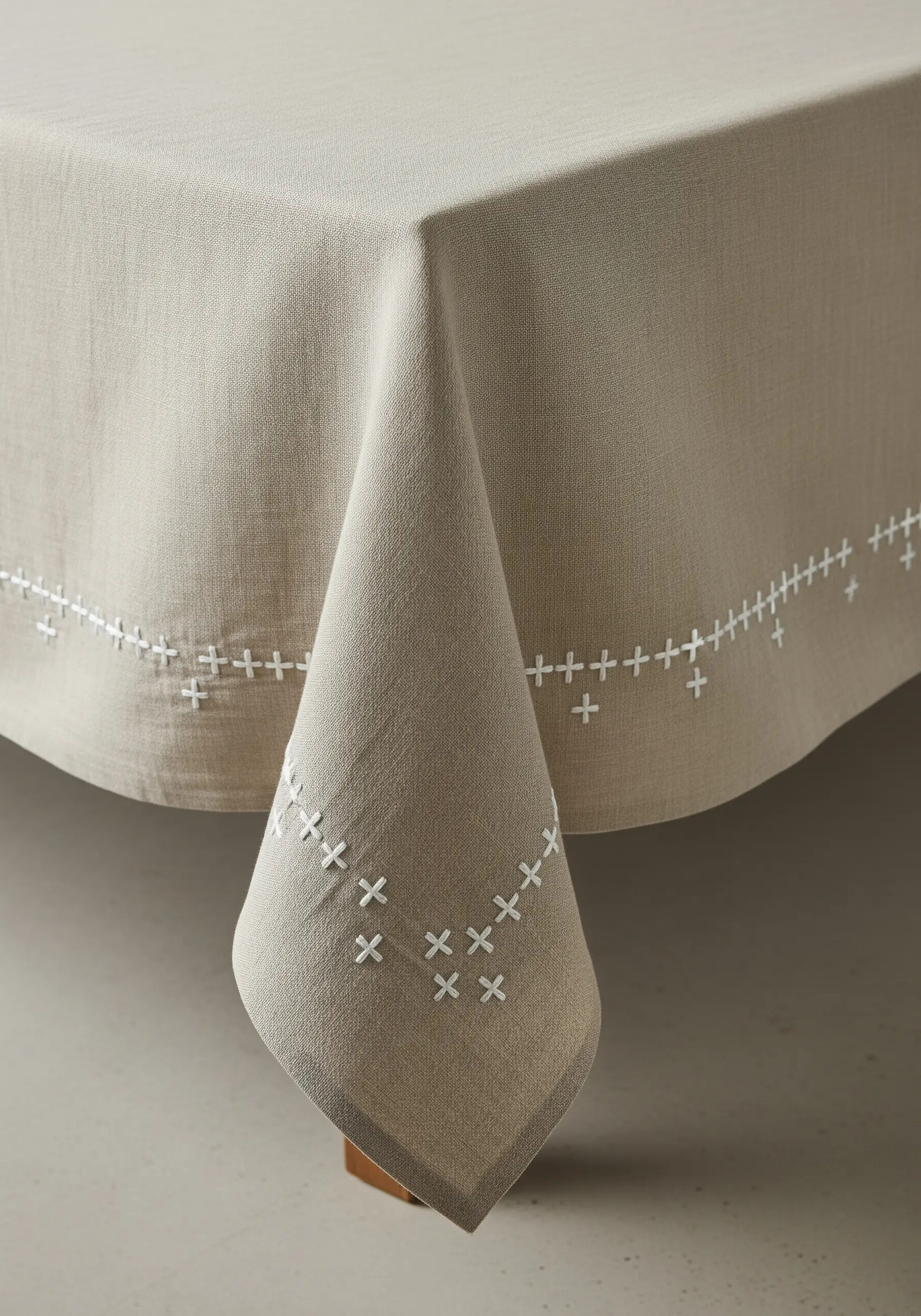 A simple, modern cross-stitch border in white thread on a neutral linen tablecloth.