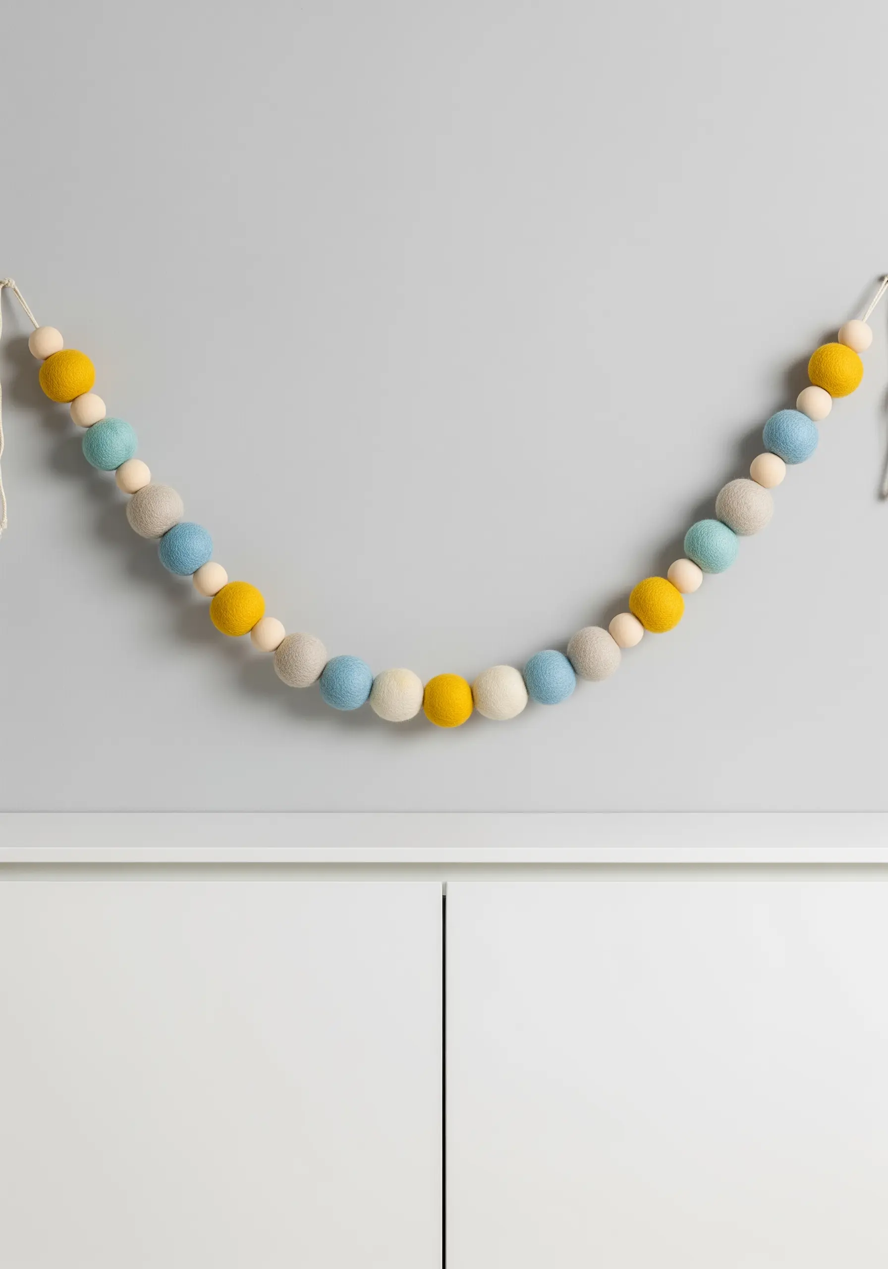 A garland of felt balls in yellow, blue, and grey, interspersed with round wooden beads.