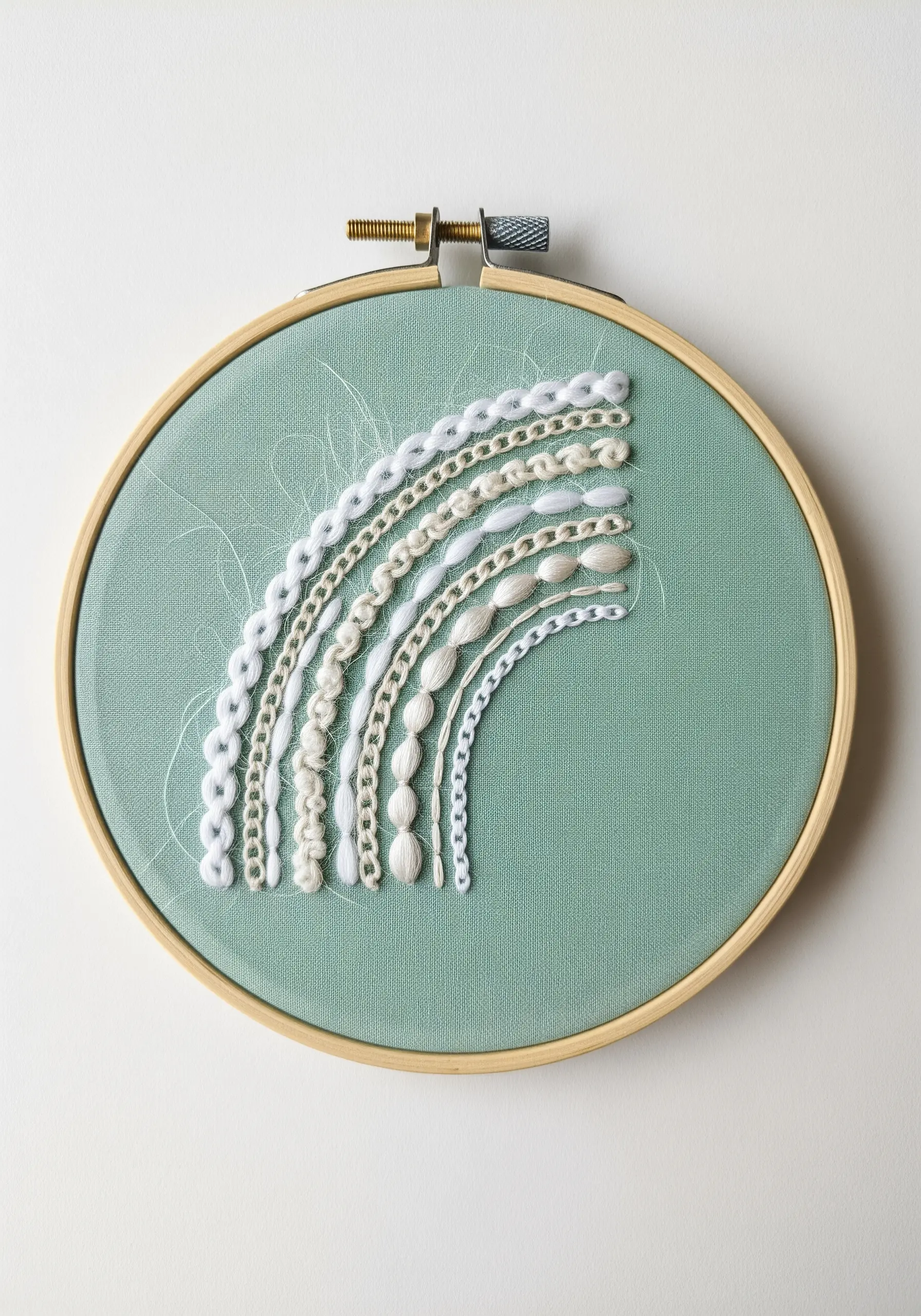 A monochrome white stitch sampler in an arc shape on sage green fabric.