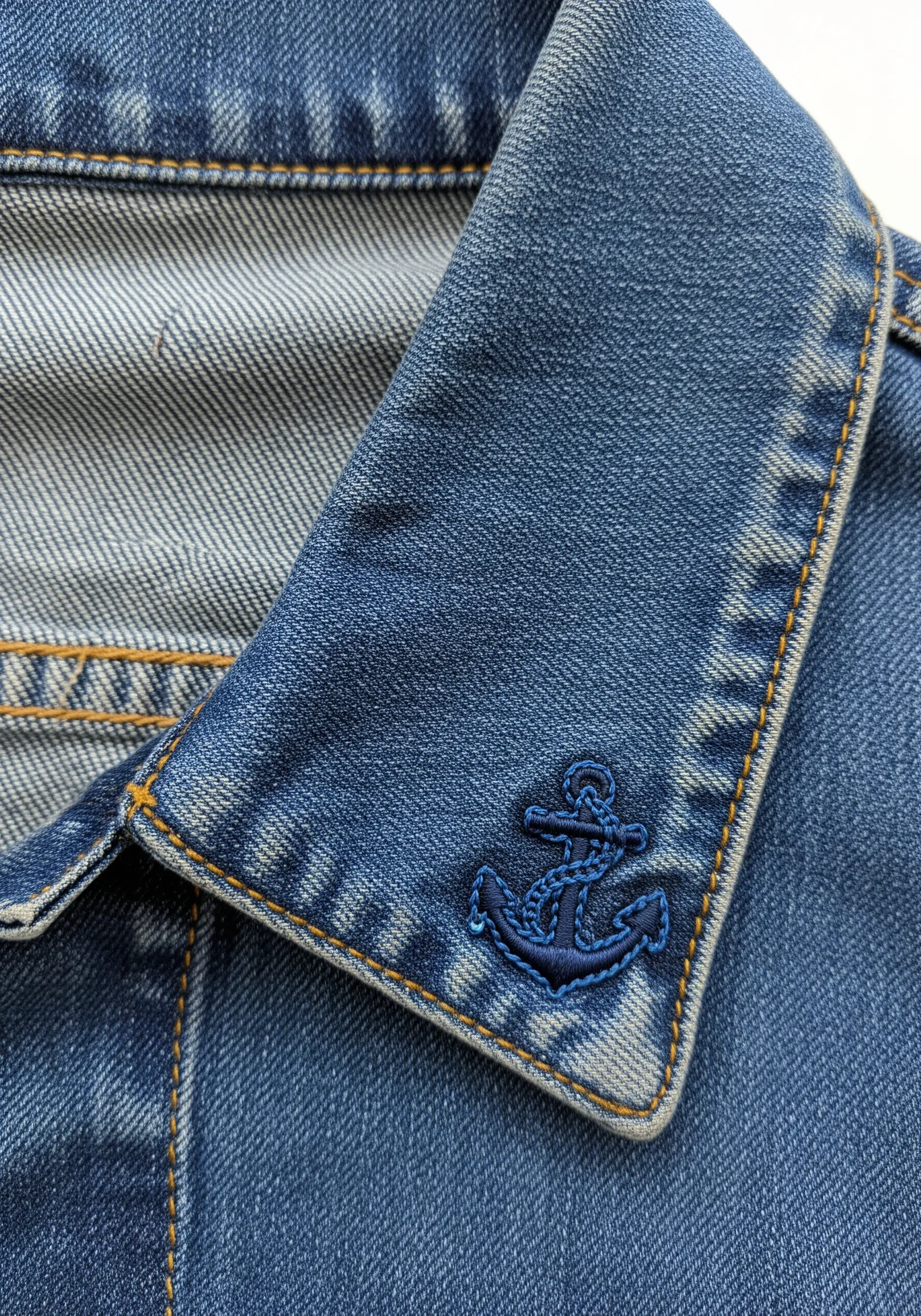 A dark blue padded satin stitch anchor embroidered on the collar of a denim jacket