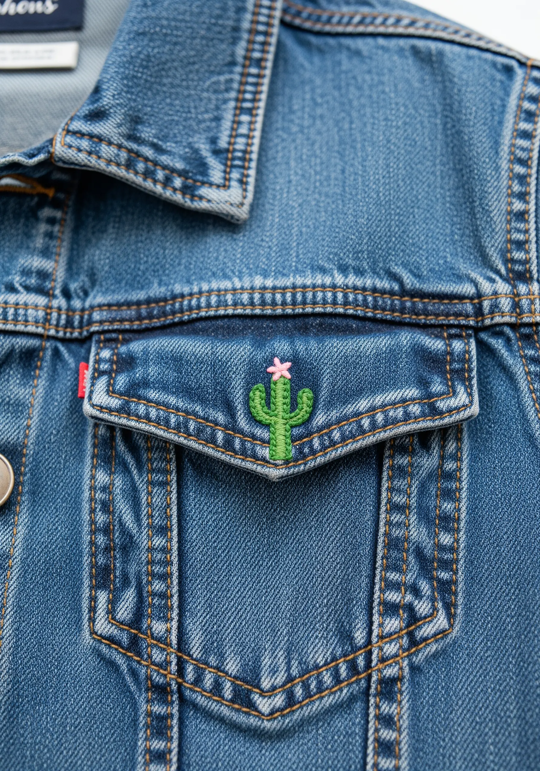 Small green embroidered cactus with a pink flower on the corner of a denim jacket pocket