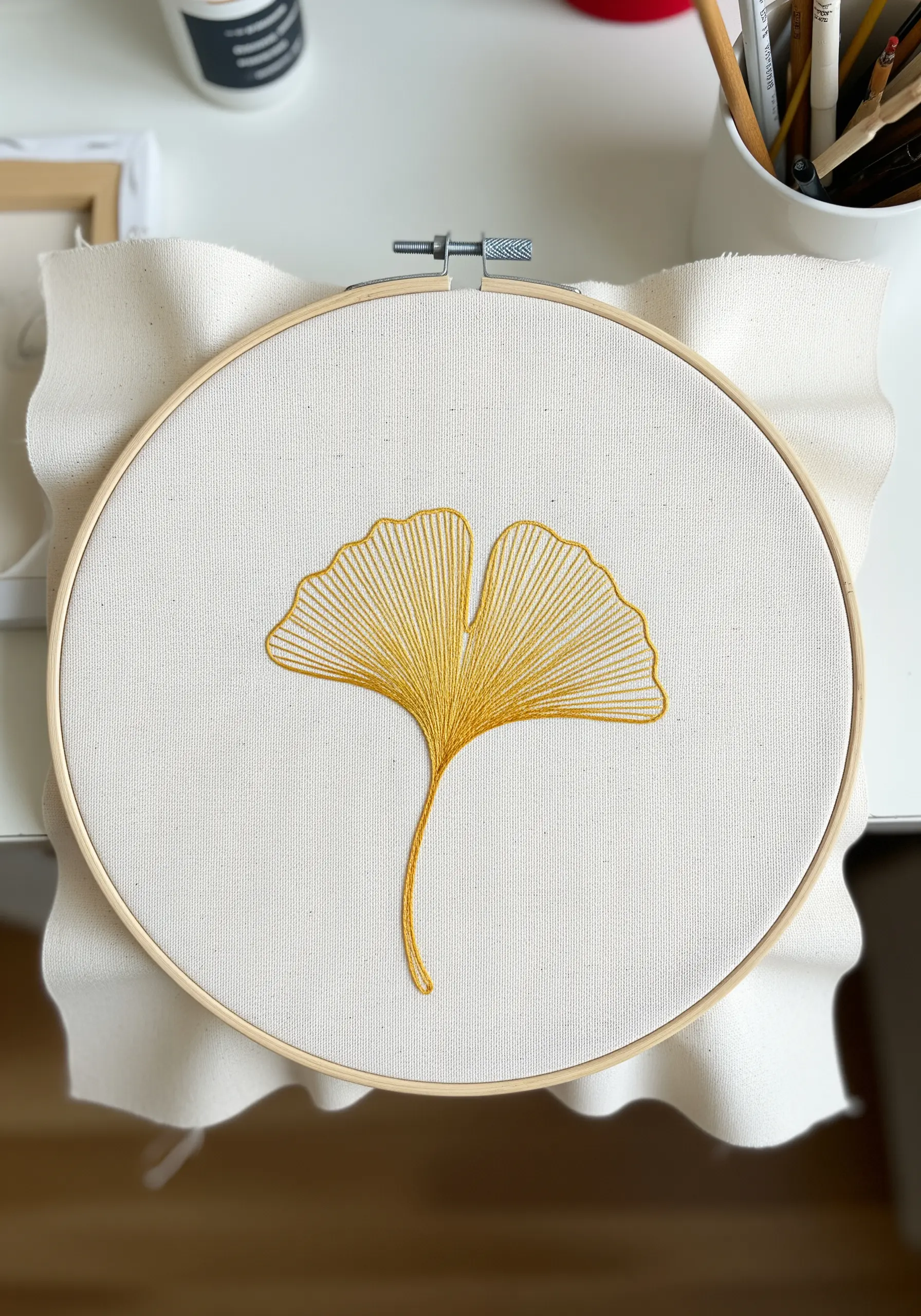 A ginkgo leaf embroidered in golden yellow thread with stitches radiating from the stem.