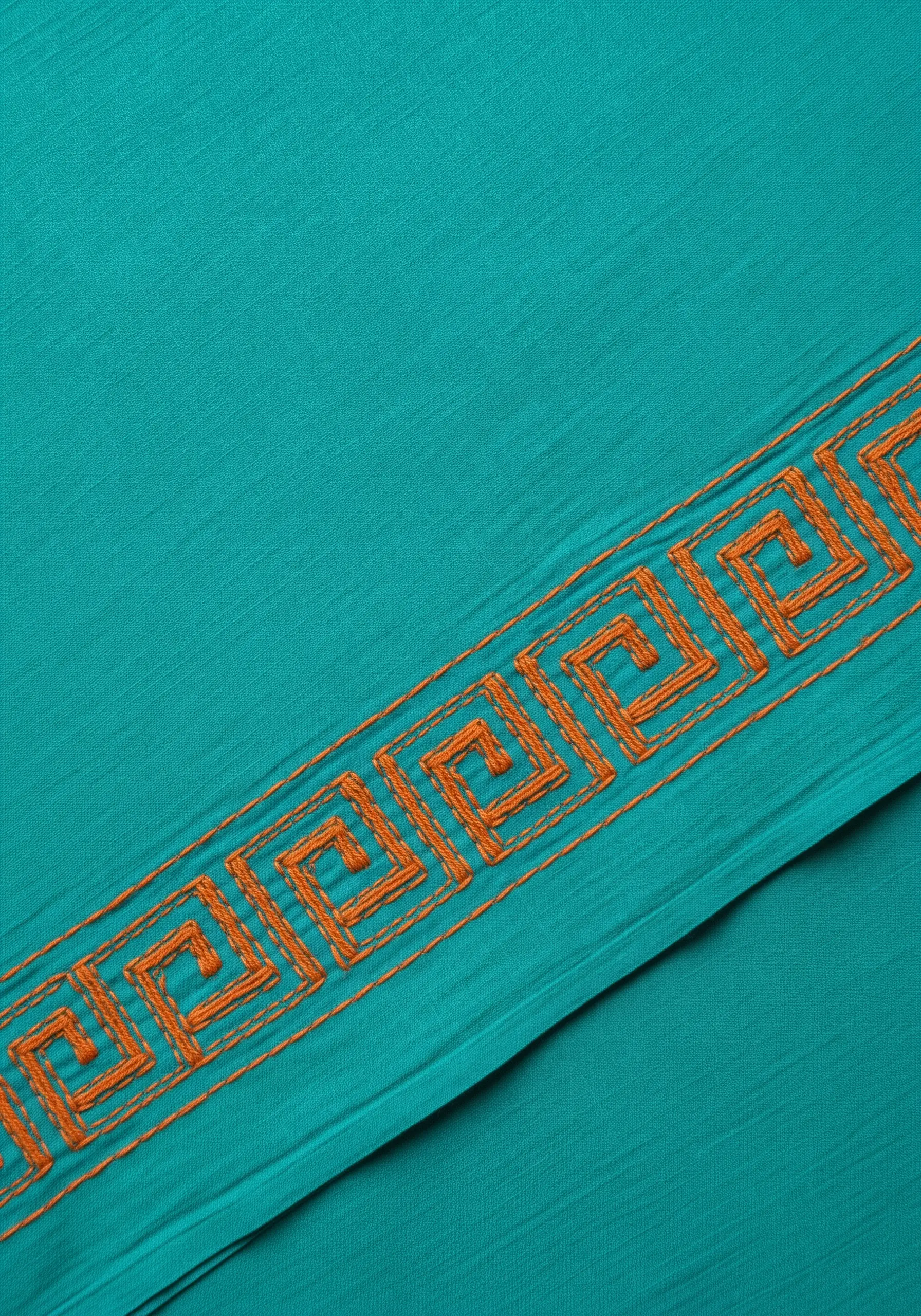 A Greek key border in orange thread on a textured teal fabric.