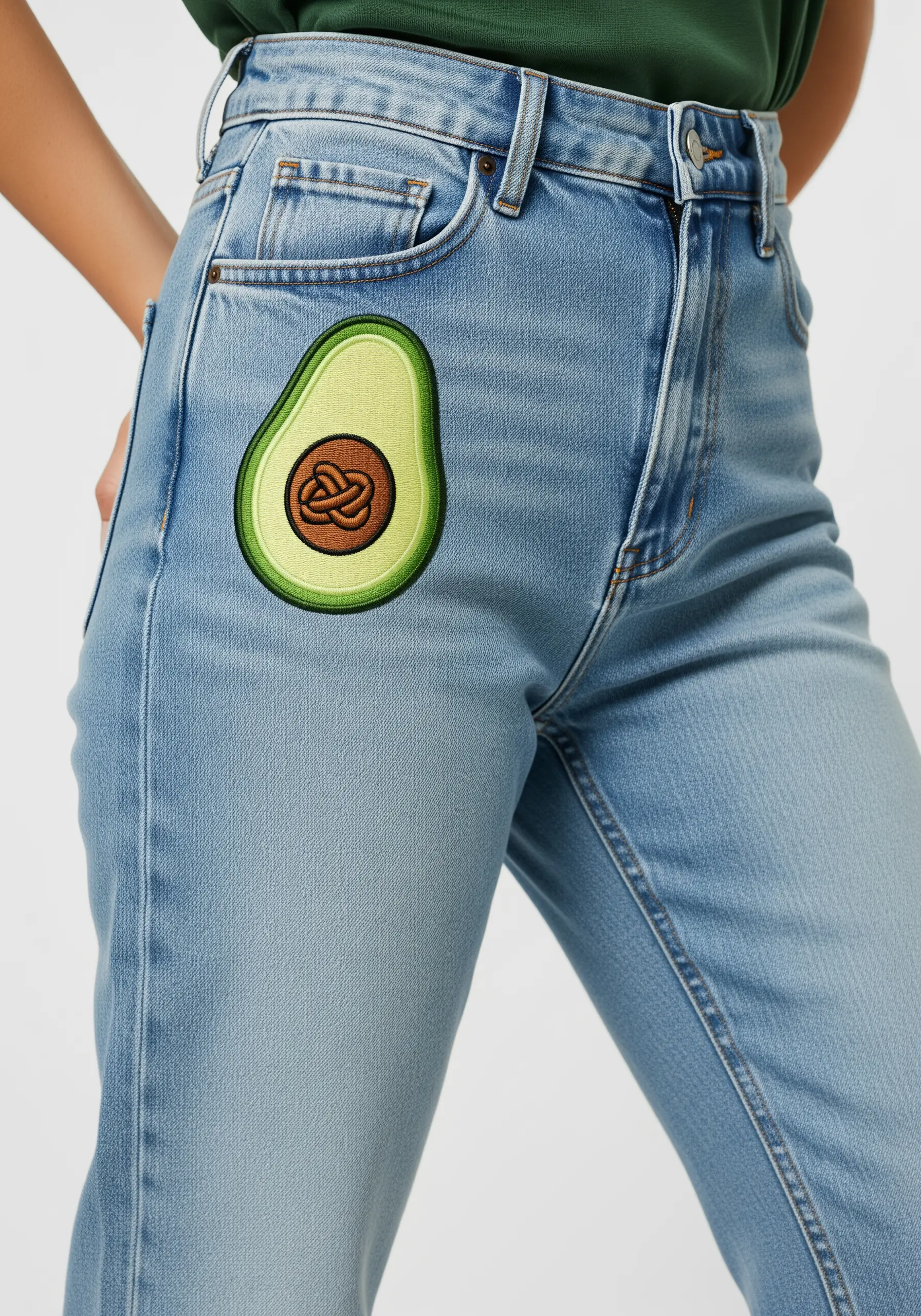 An embroidered avocado half with a textured pit on light wash denim.