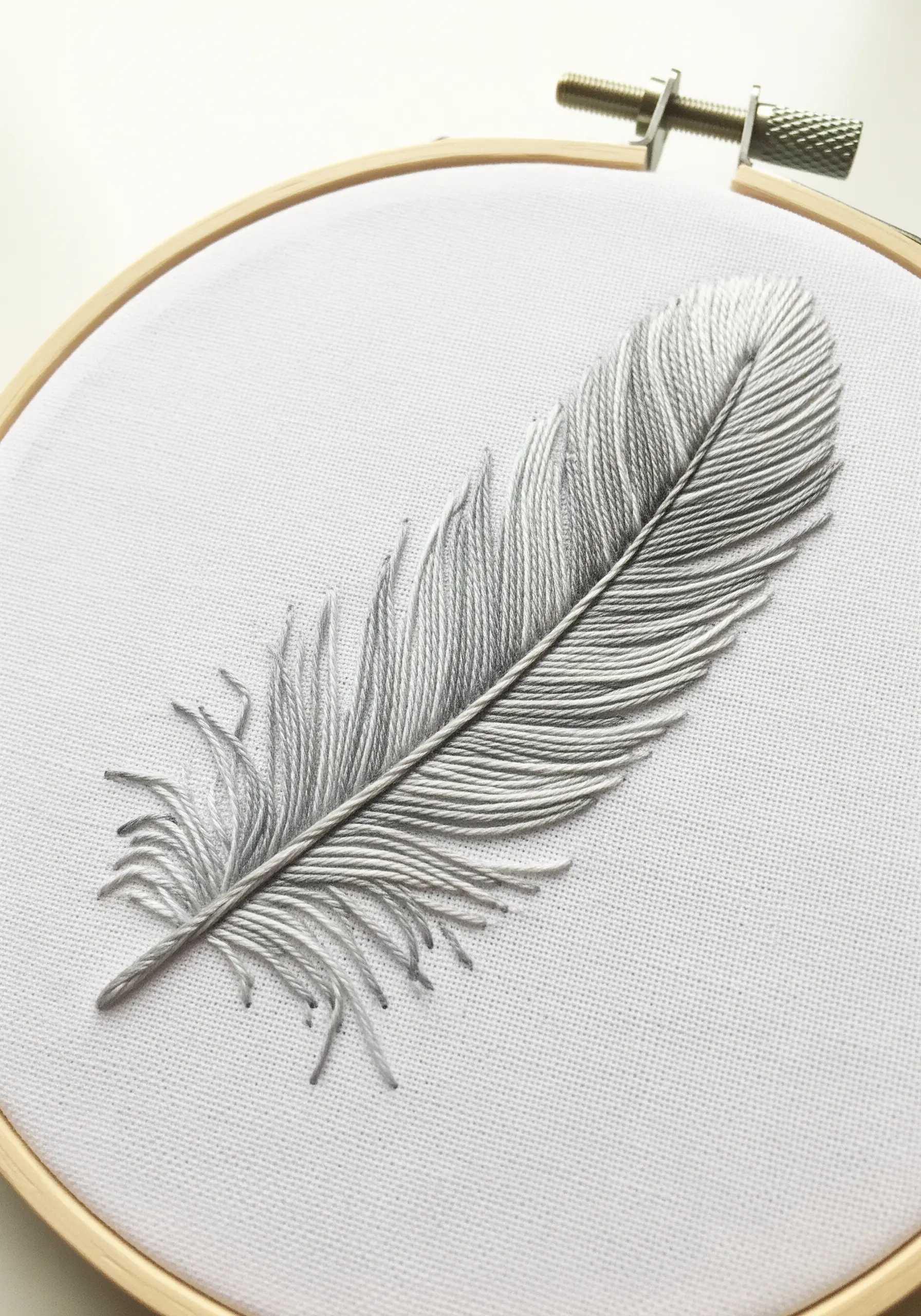 A realistic grey feather created with carefully angled satin stitches on white fabric.