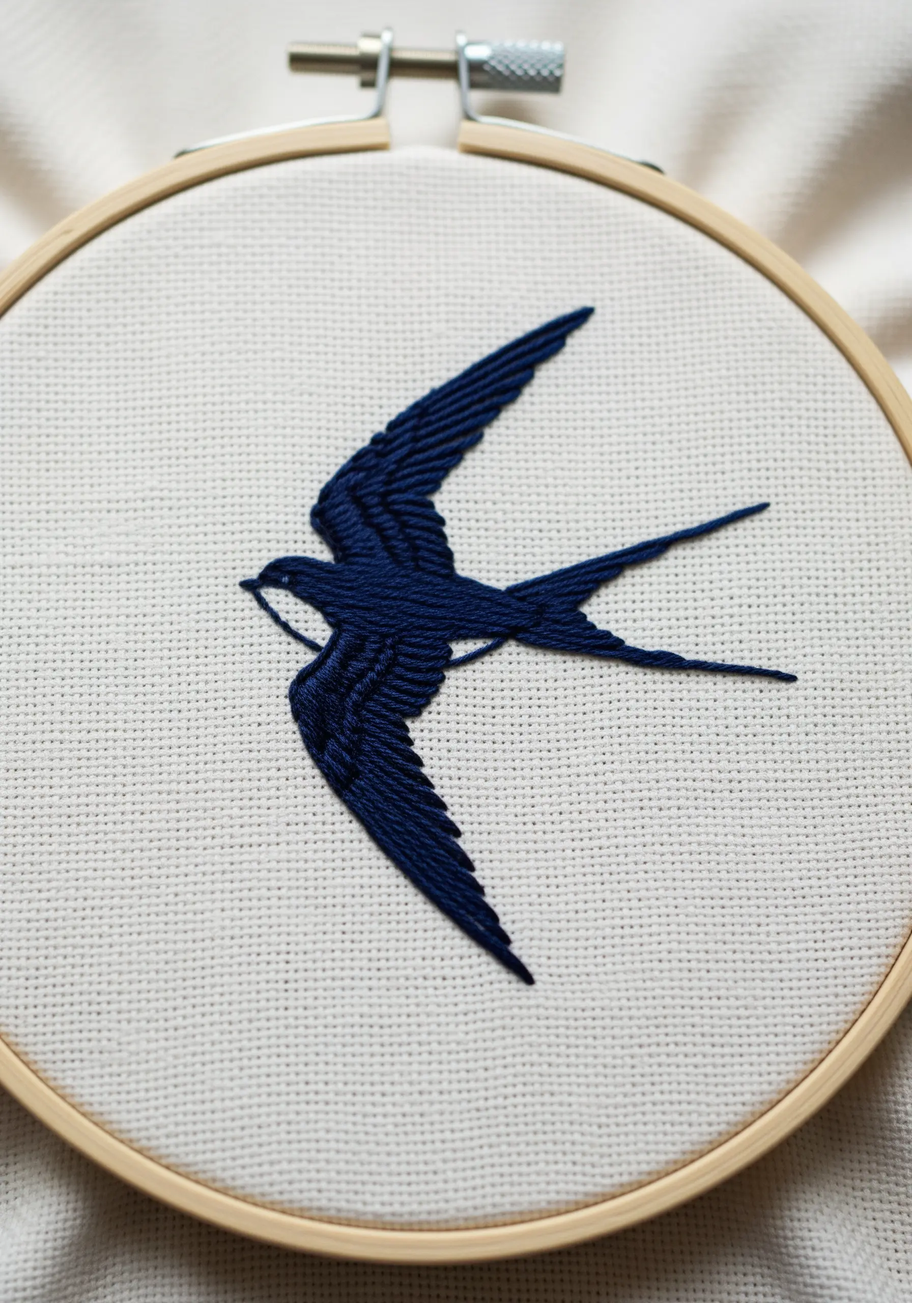 A solid navy blue silhouette of a swallow embroidered using split stitch fill.