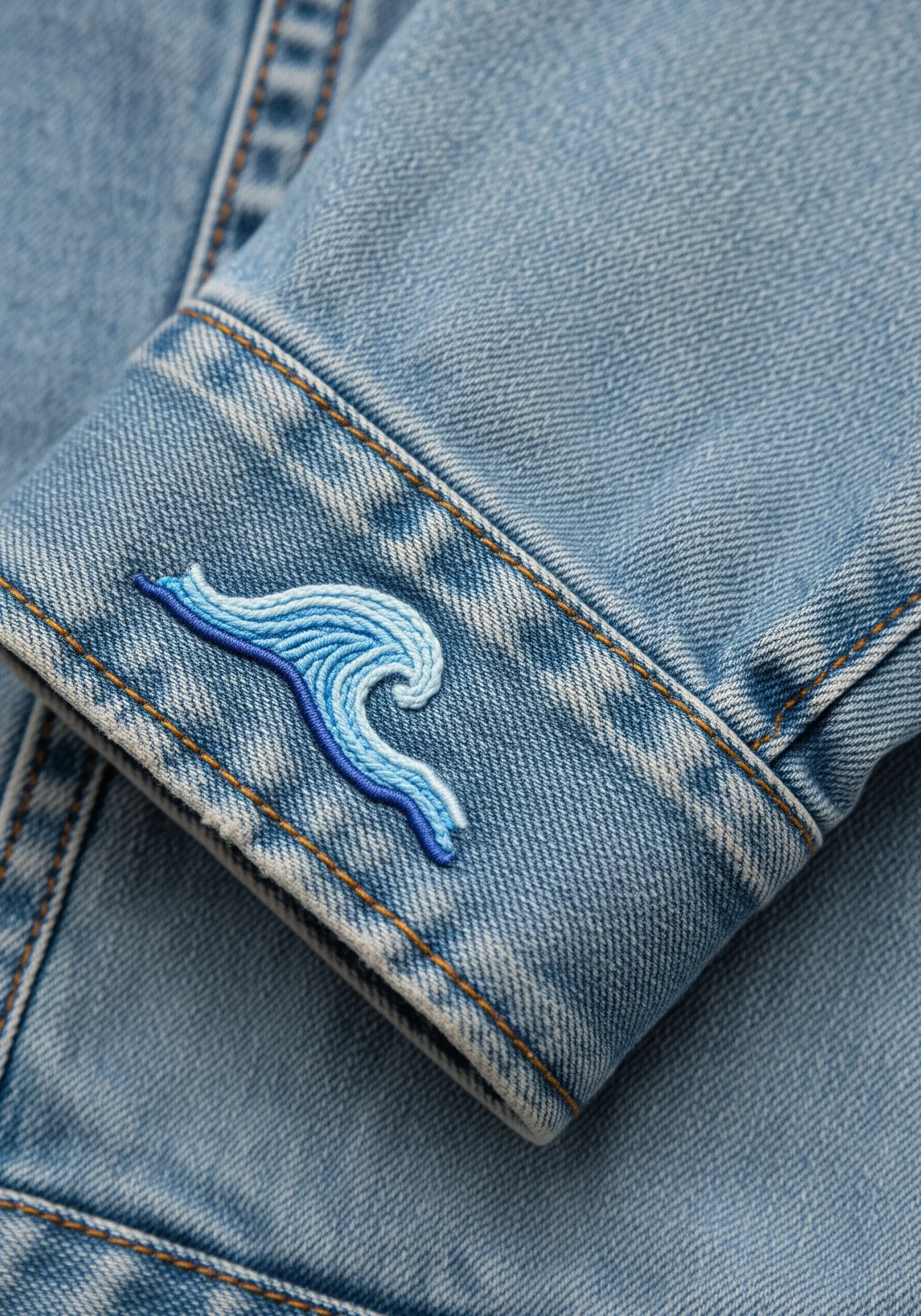 A stylized ocean wave embroidered on a denim cuff using three shades of blue