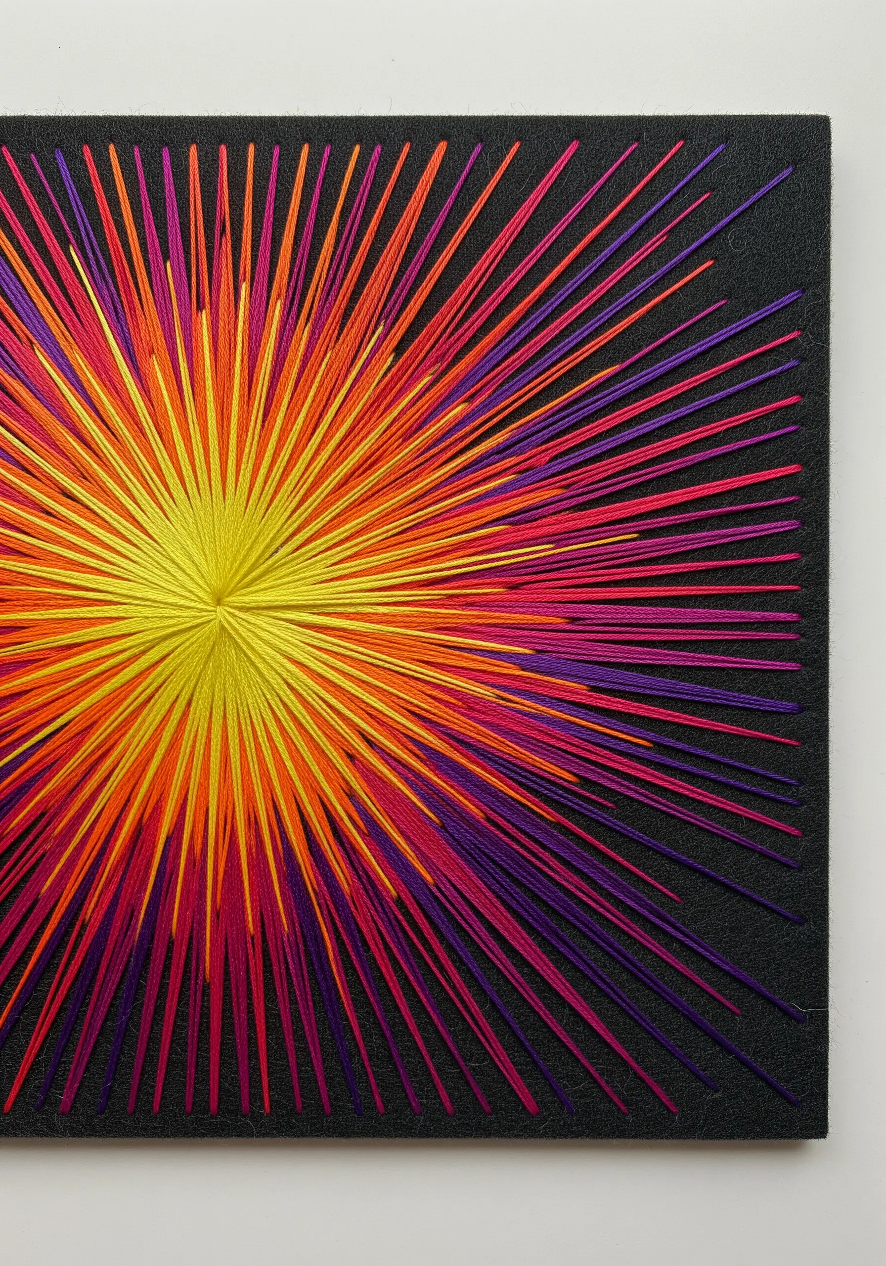 Vibrant thread burst embroidery in yellow, orange, and purple on black canvas.