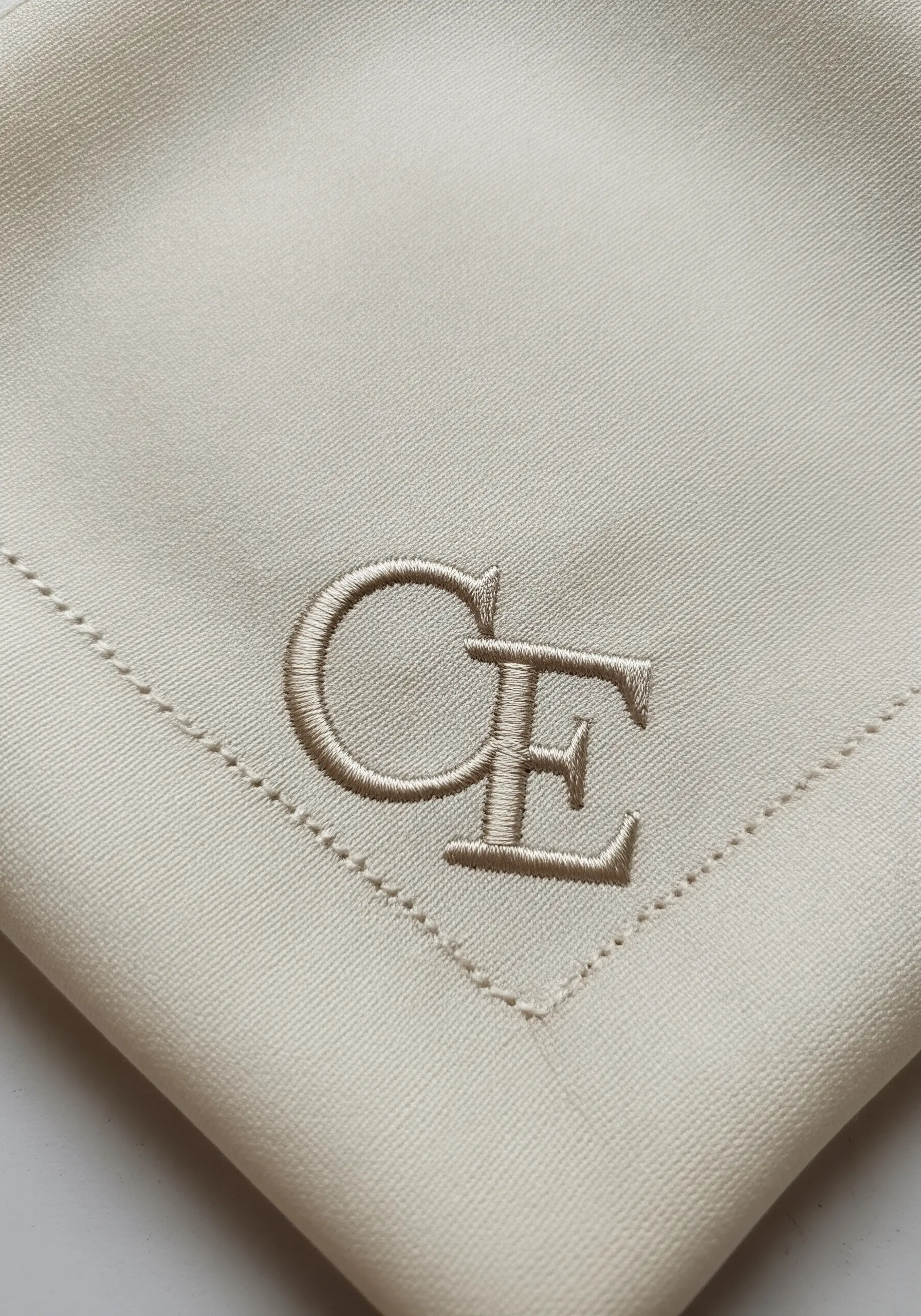 Interlocking 'CE' monogram in beige satin stitch on a beige napkin.