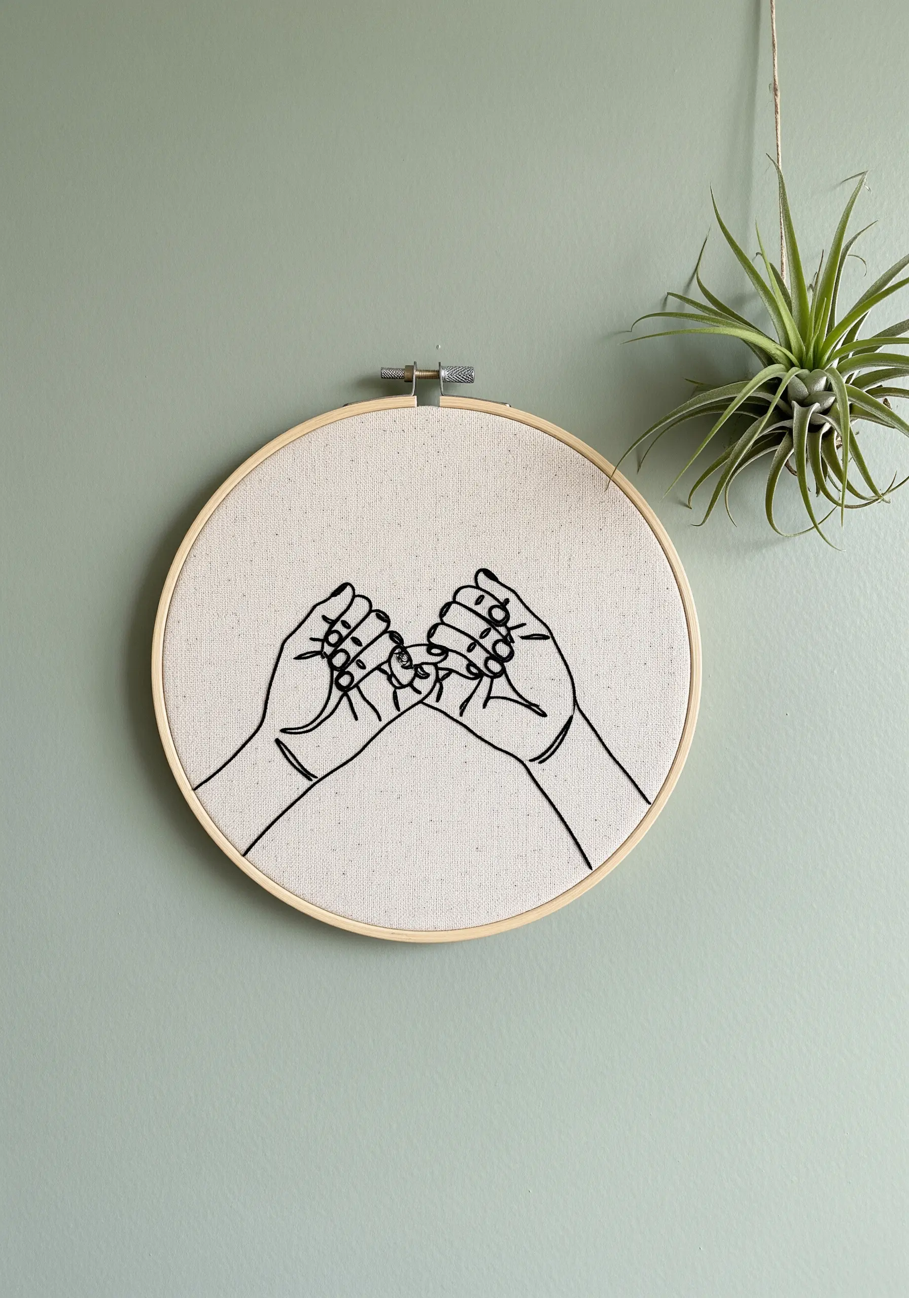 Clean black line art embroidery of a pinky promise gesture in a wooden hoop.