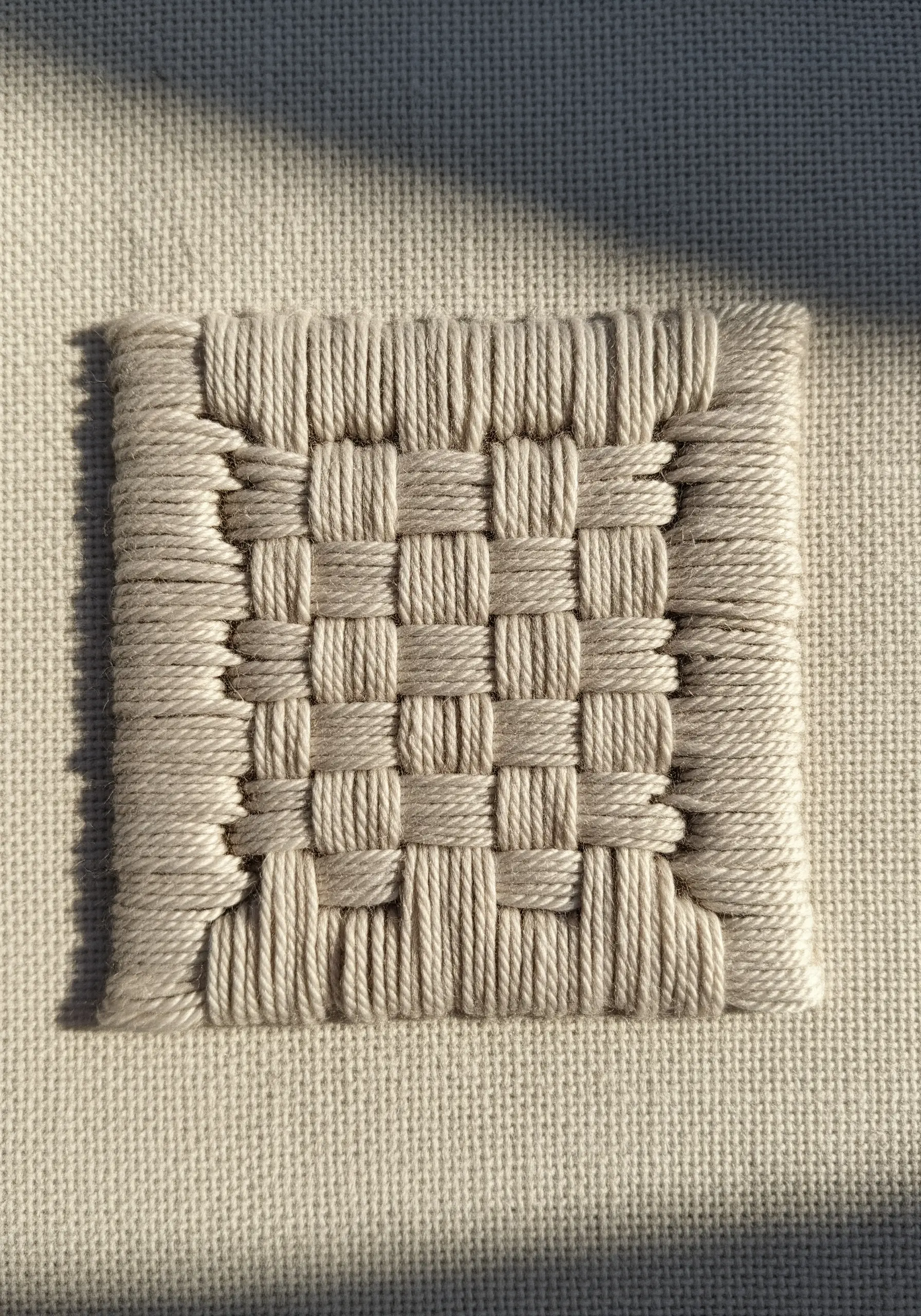 A small woven square created with off-white thread on neutral fabric.