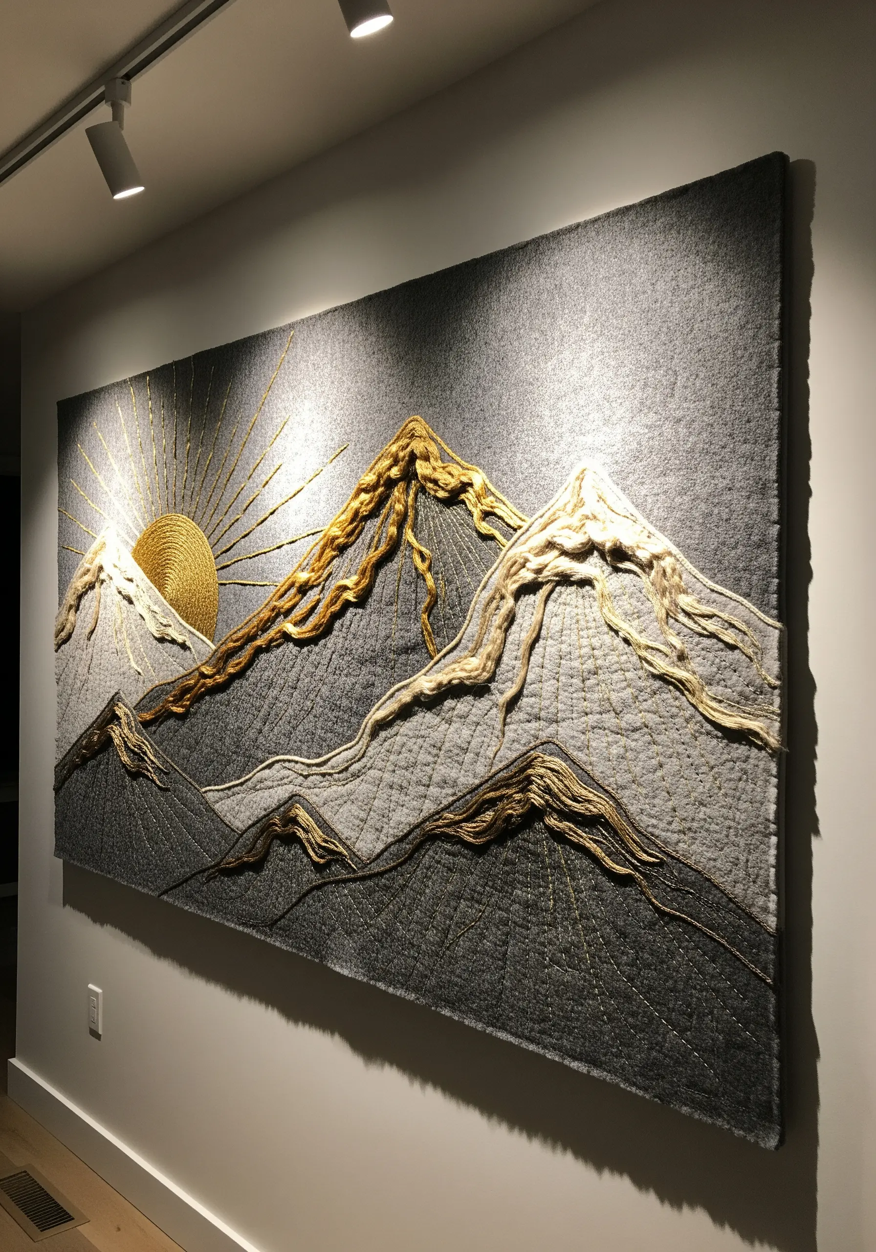 Large embroidered mountain landscape with gold, silver, and white thread on grey fabric.