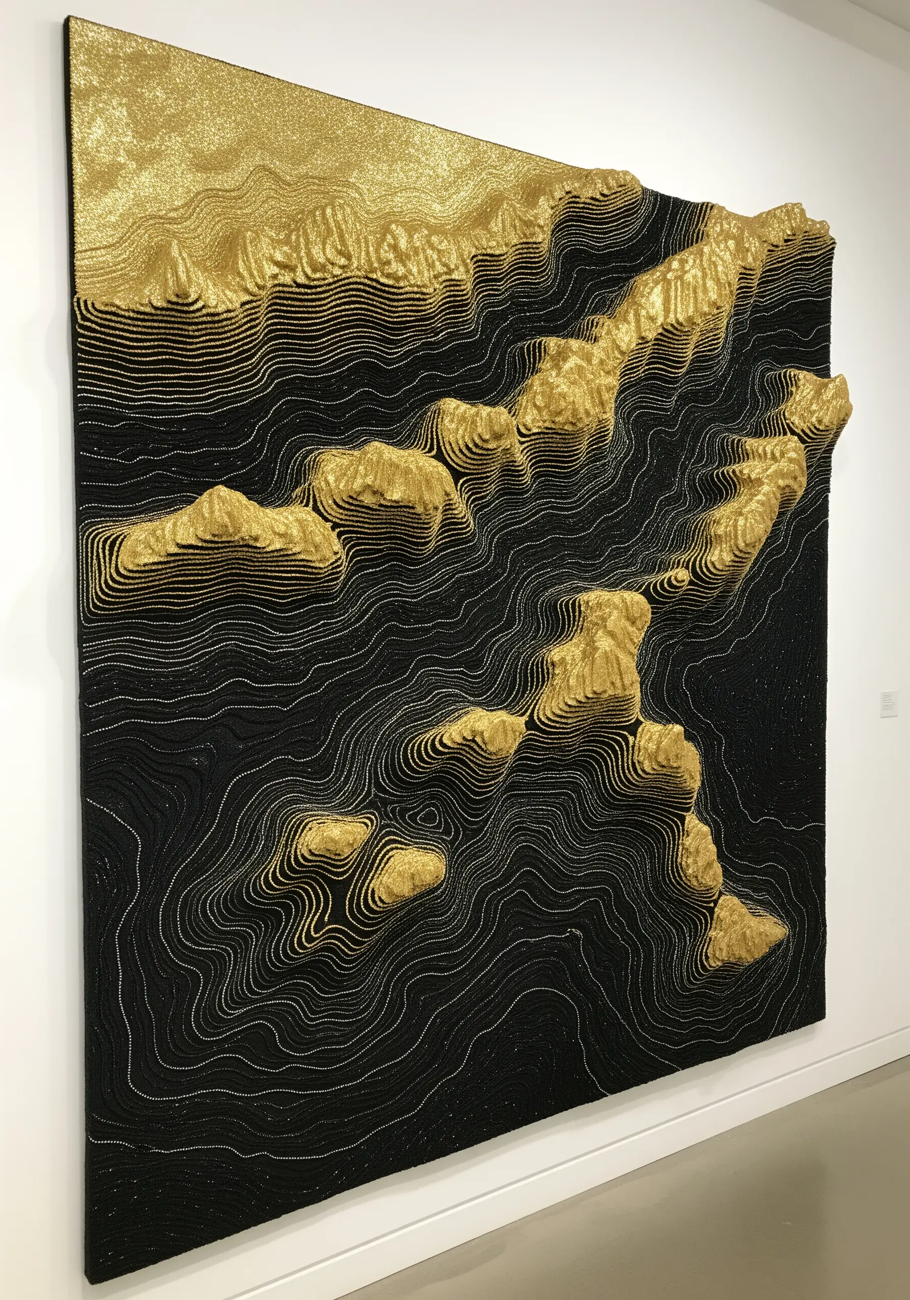 A large, 3D topographical map made from layered black and gold thread.