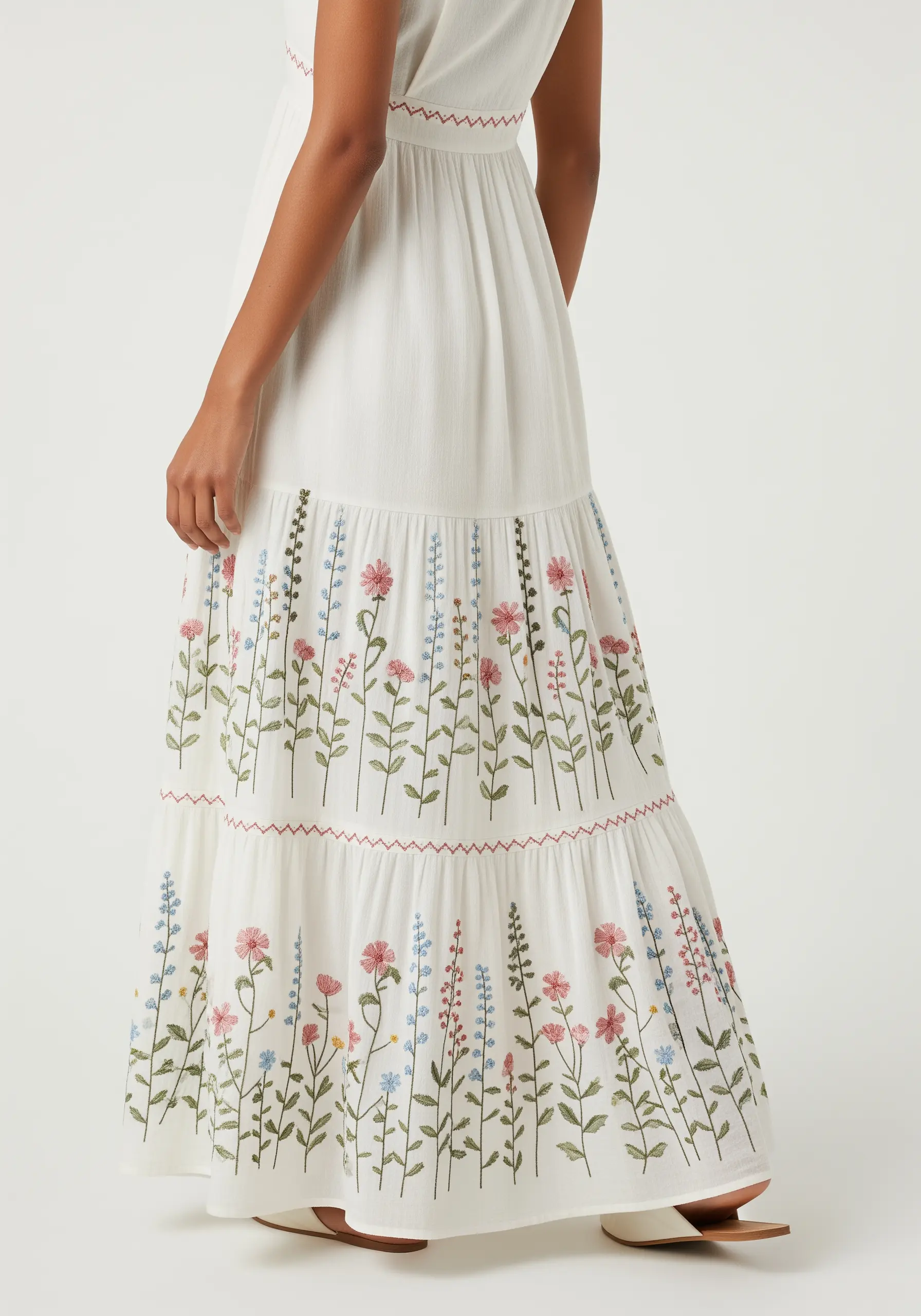 Delicate wildflower embroidery in pink, blue, and green on the tiered skirt of a white maxi dress.
