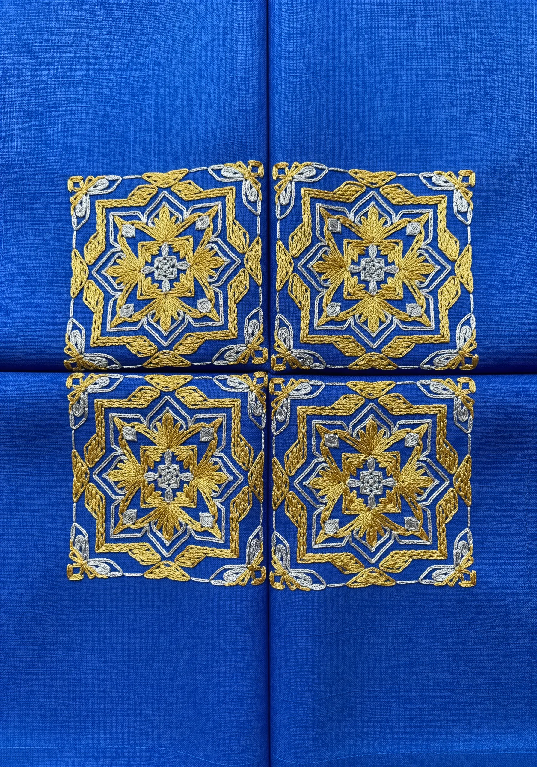 Four geometric floral motifs embroidered in gold and silver metallic thread on cobalt blue fabric.