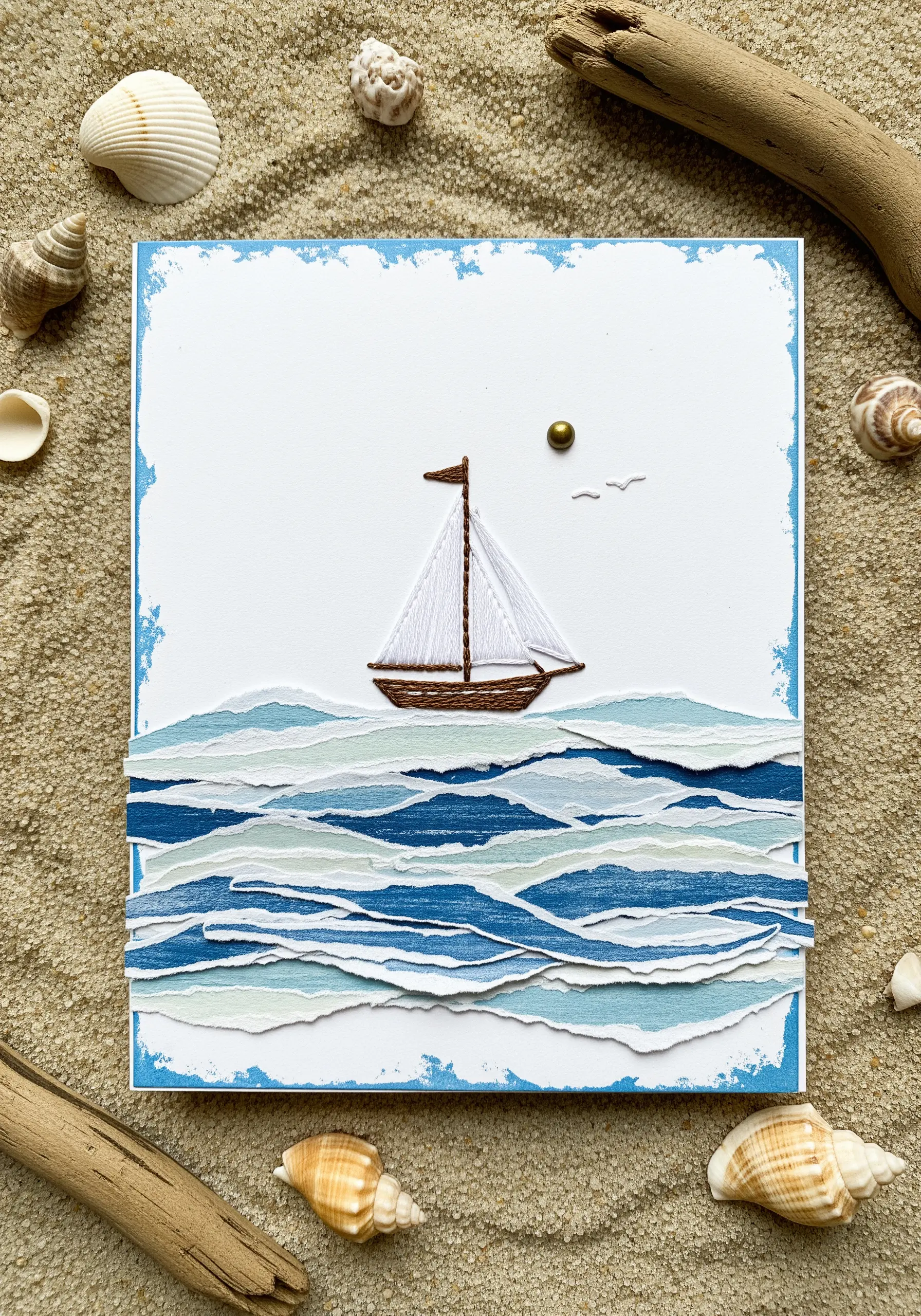 A sailboat with embroidered sails floating on waves made from layered torn blue paper.