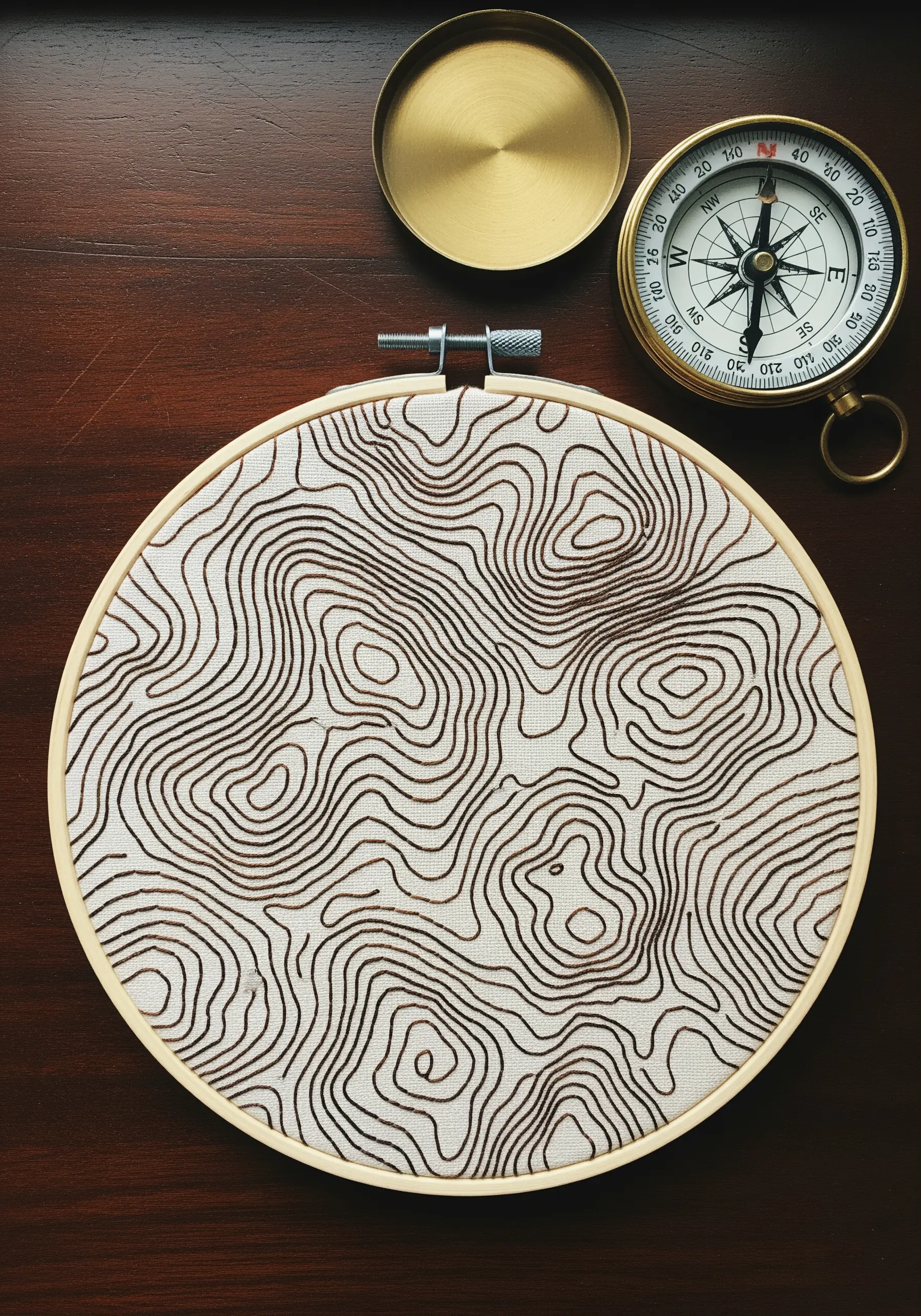 A topographic map pattern stitched with brown thread on natural linen in a hoop.