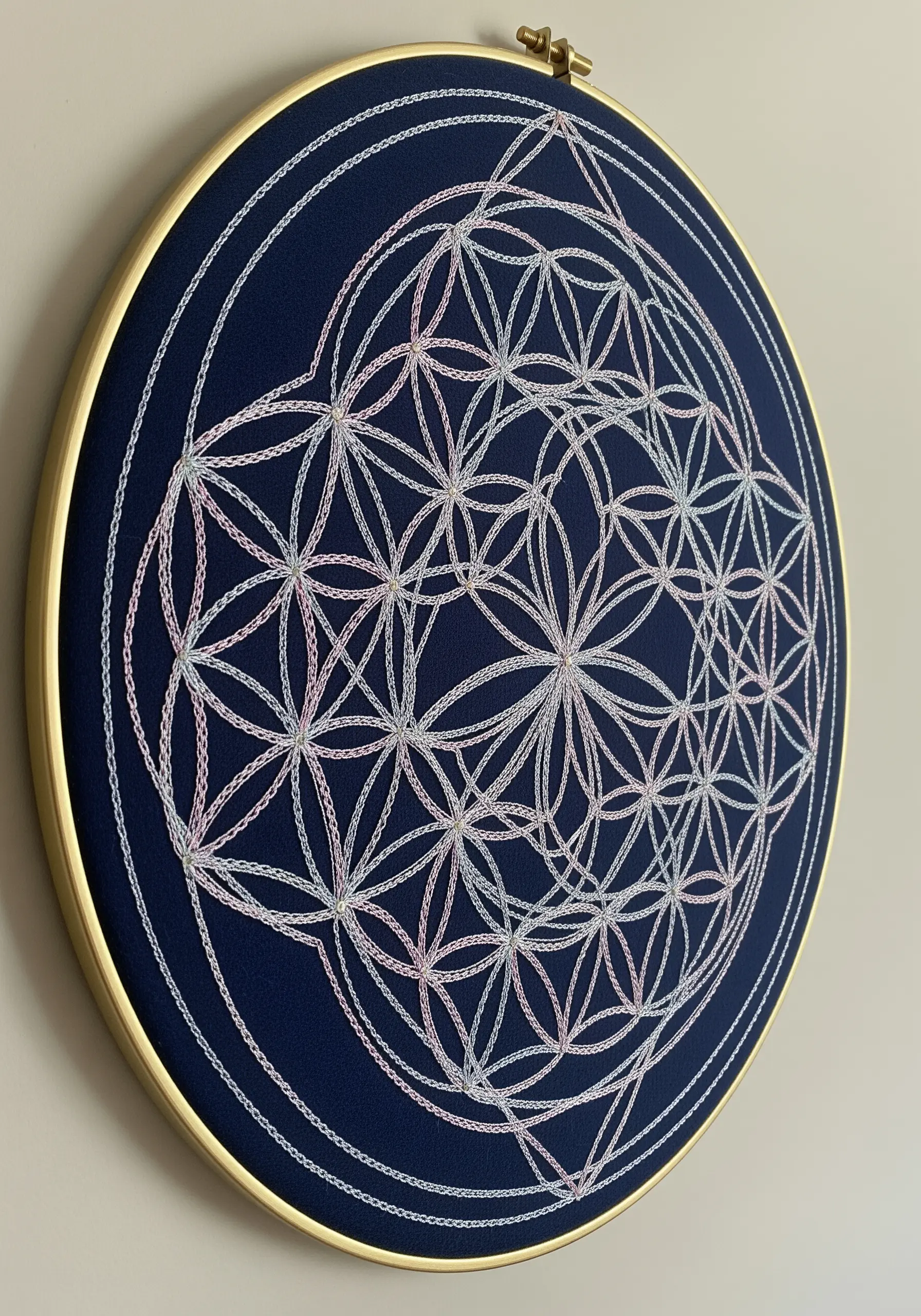 The Flower of Life sacred geometry pattern stitched in iridescent thread on navy blue fabric.
