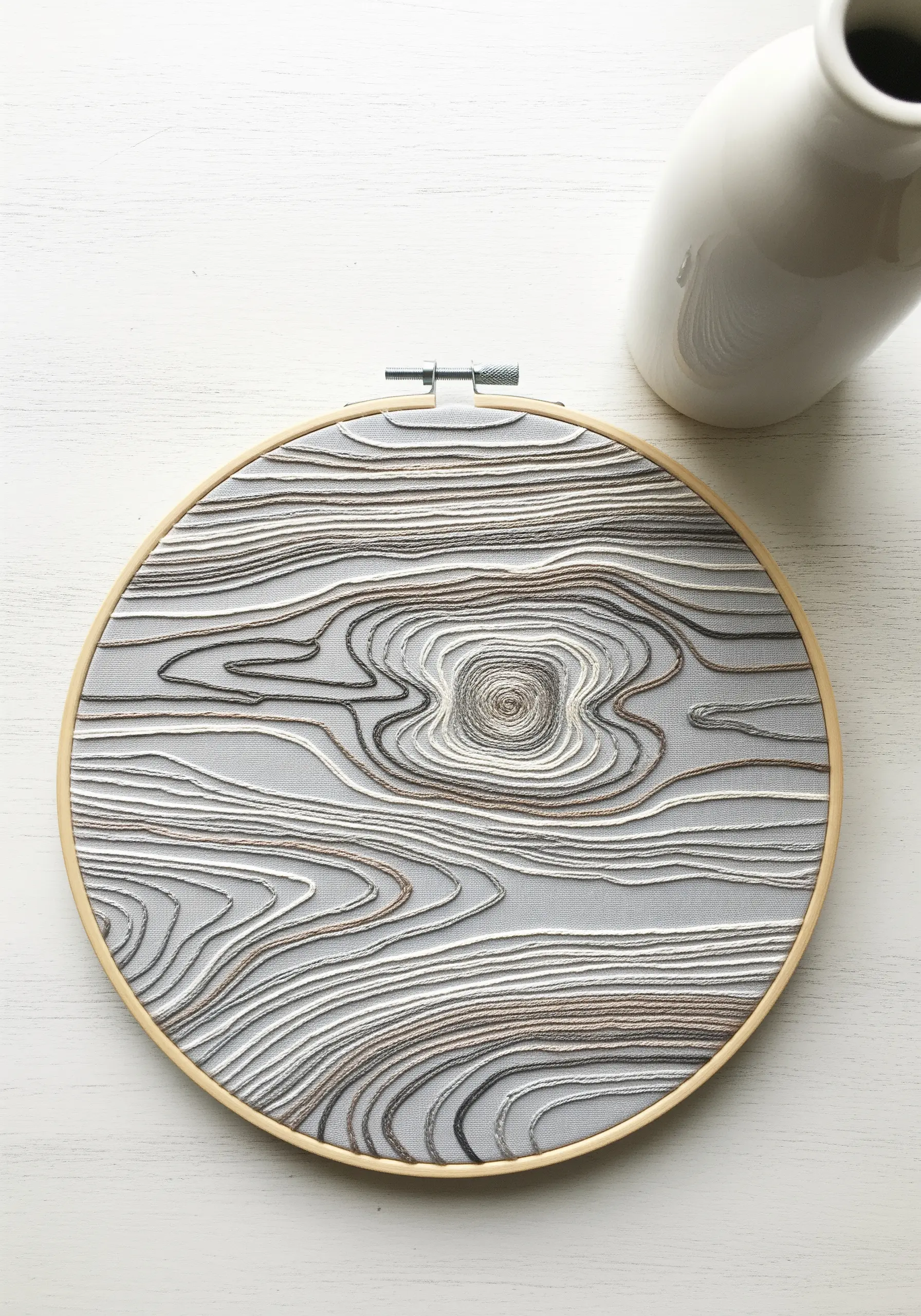 Embroidery hoop with a detailed wood grain pattern in white, grey, and brown thread.