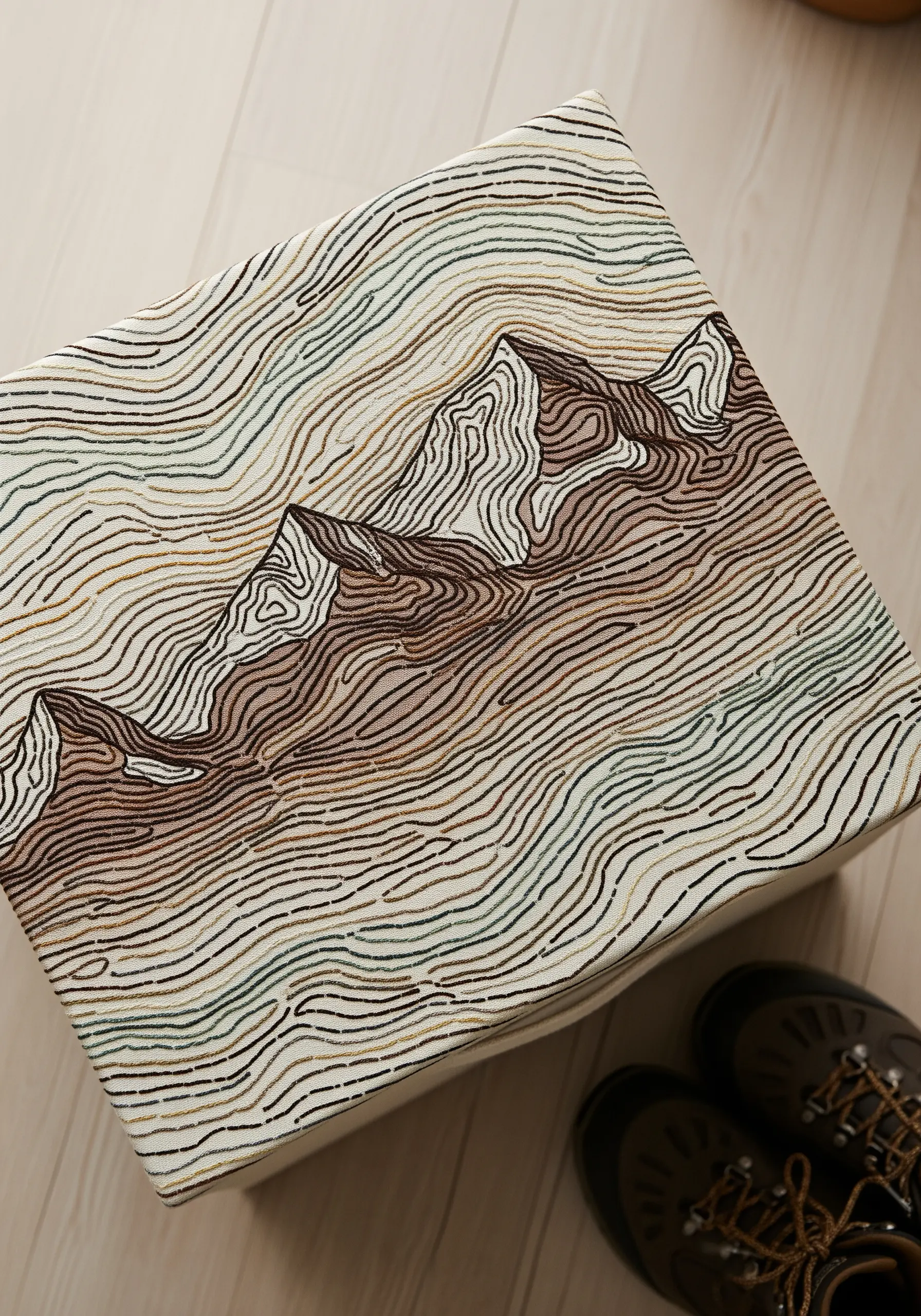 Upholstered stool with a dense, topographic line pattern embroidered in earthy tones.