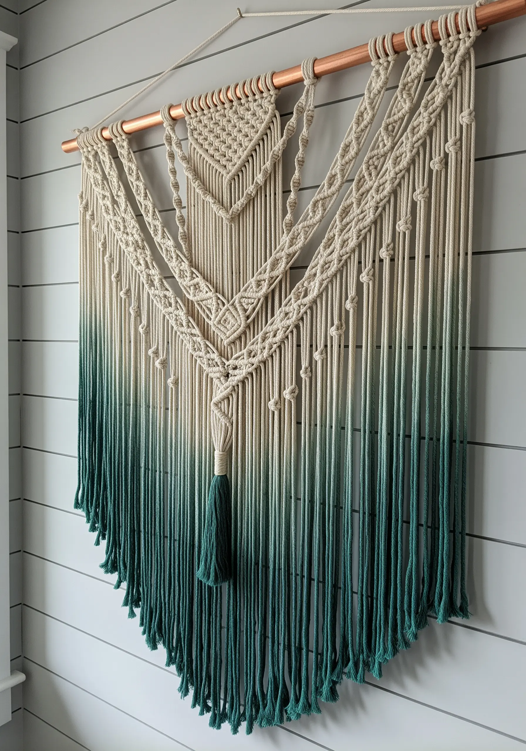 A large macrame wall hanging with cords dip-dyed in a gradient of deep green.