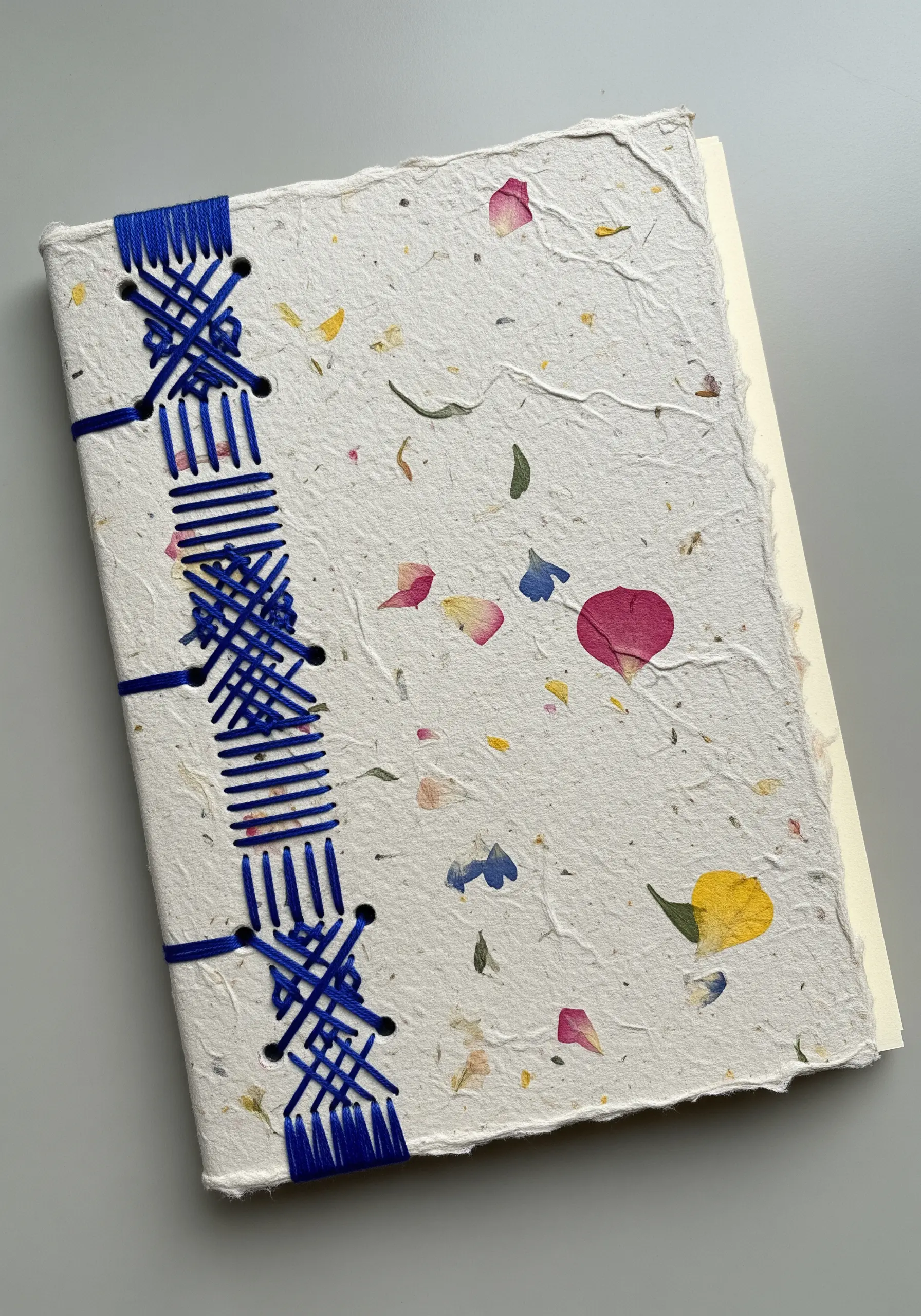 A handmade book with a decorative blue coptic stitch binding on the spine.