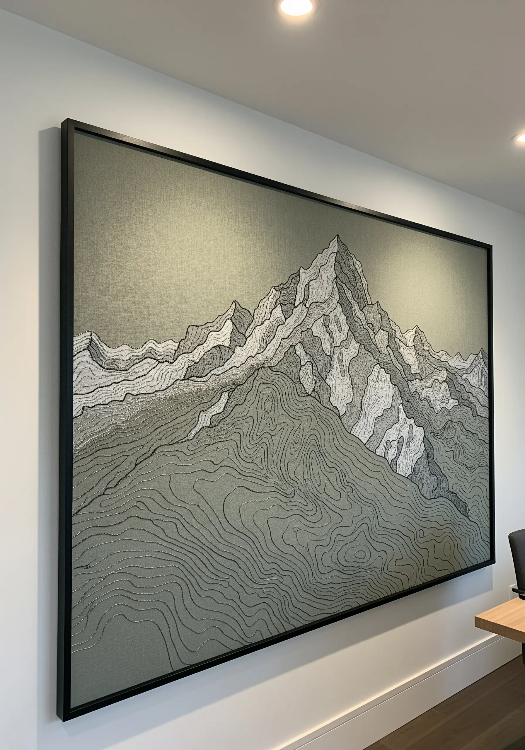 A very large, framed embroidery of a mountain range with detailed topographic line work.
