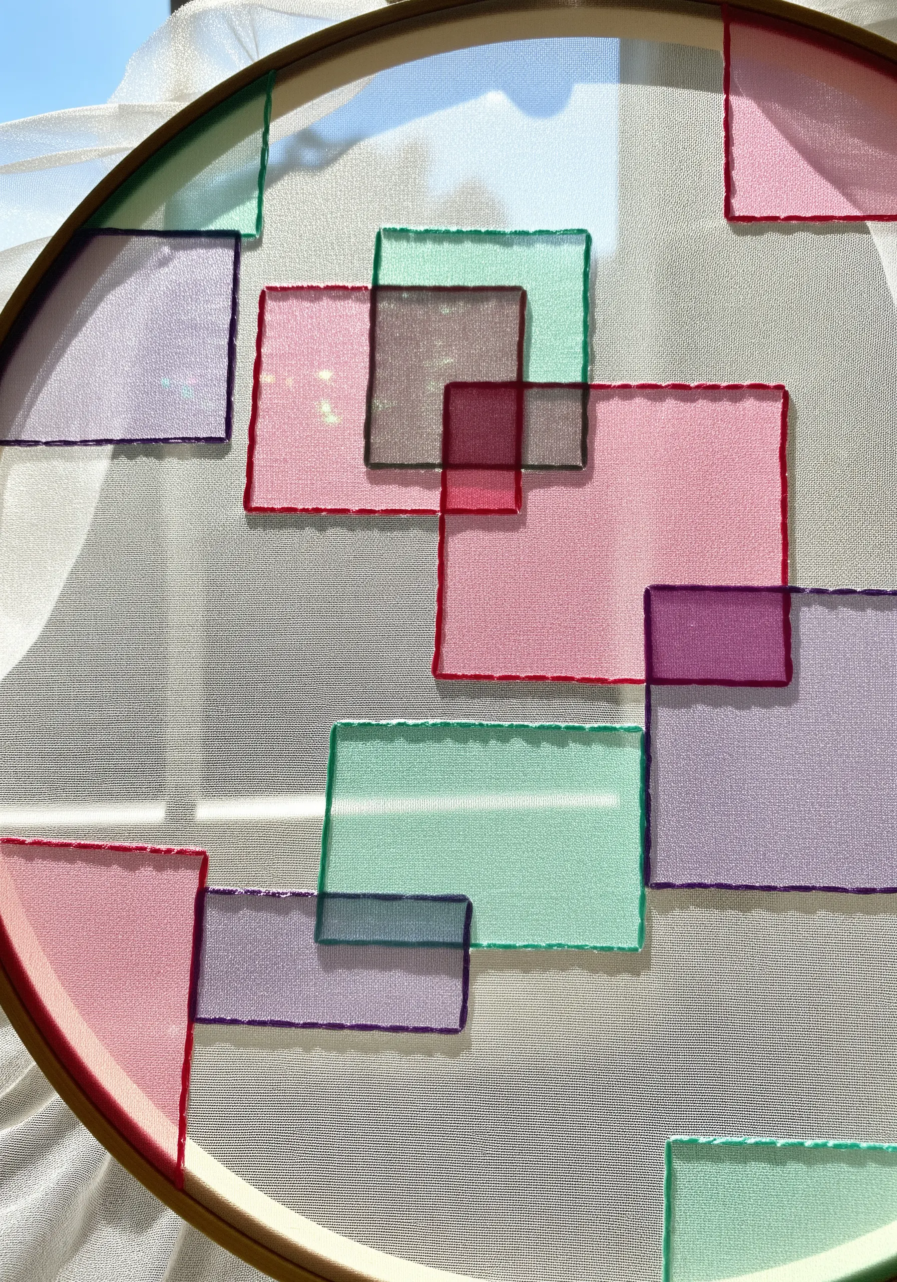 Overlapping geometric shapes stitched onto sheer fabric, creating color blends.