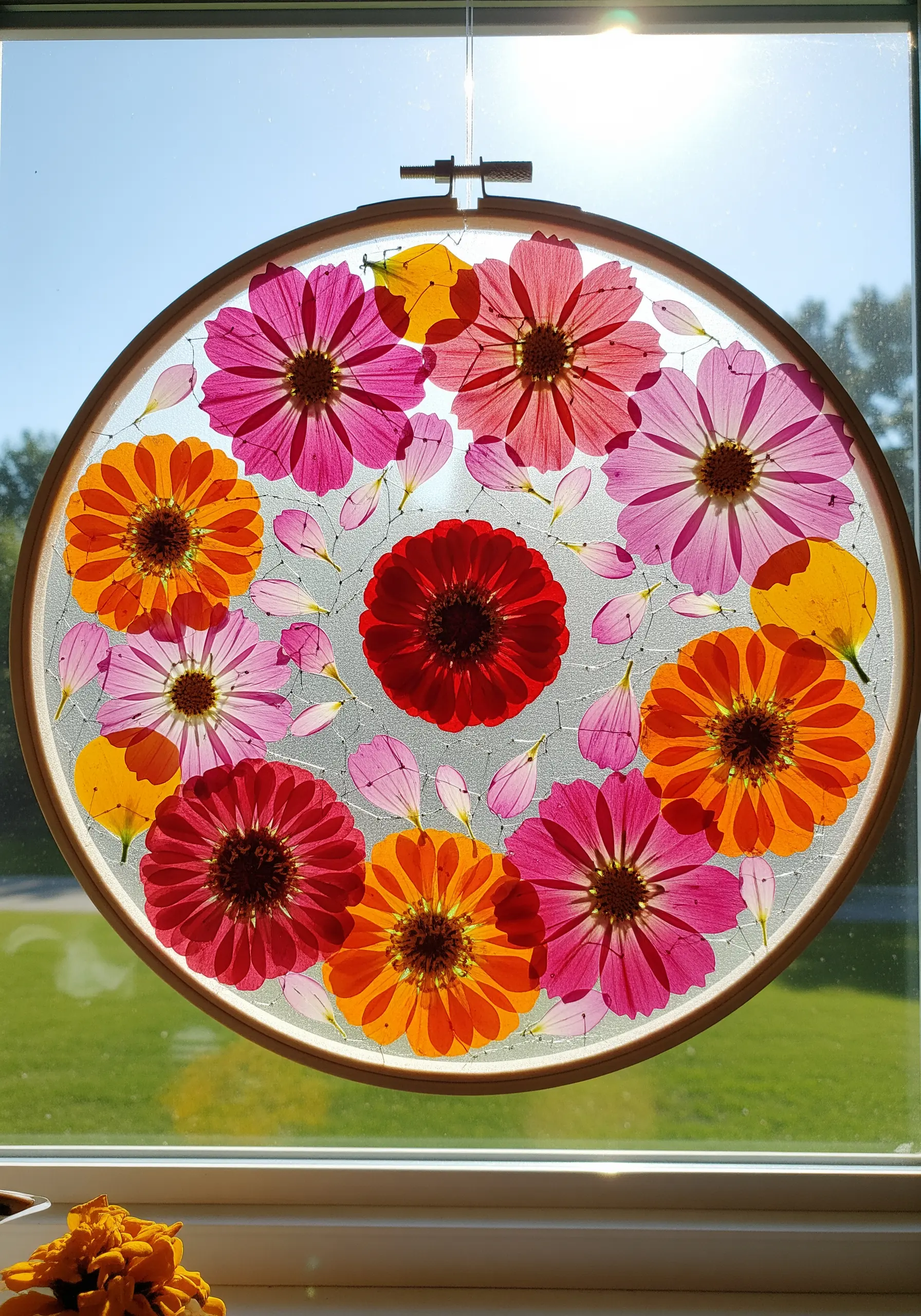 A suncatcher made with colorful pressed flowers layered in tulle inside an embroidery hoop.