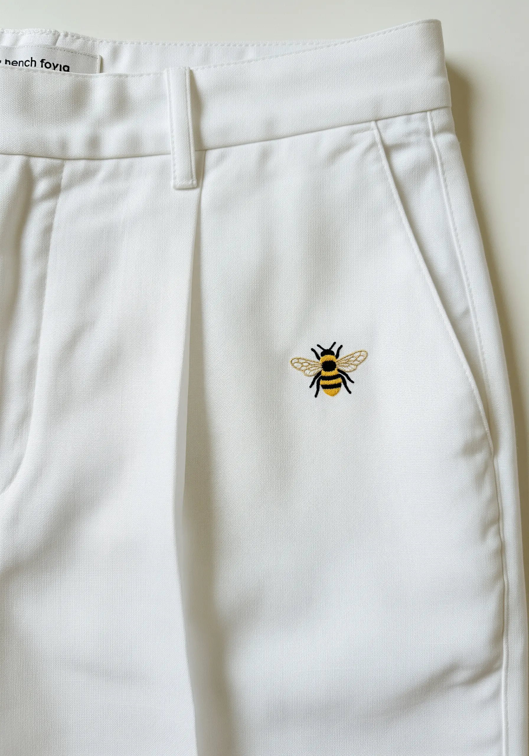 A single, realistically embroidered bee on the pocket of white trousers.