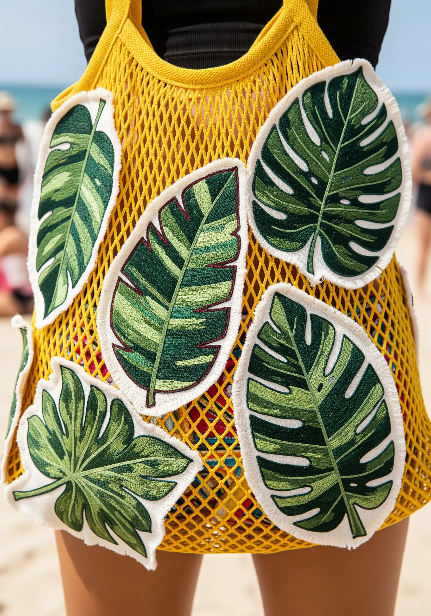 Several embroidered leaf patches with frayed edges sewn onto a yellow mesh beach bag.