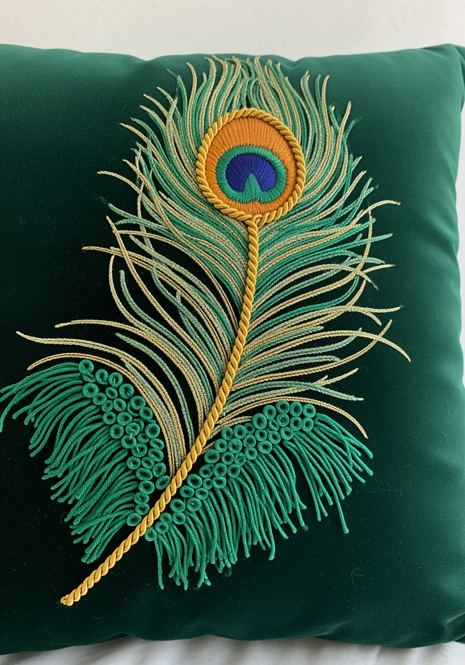 A detailed peacock feather embroidered on a green velvet cushion using un-spun floss.
