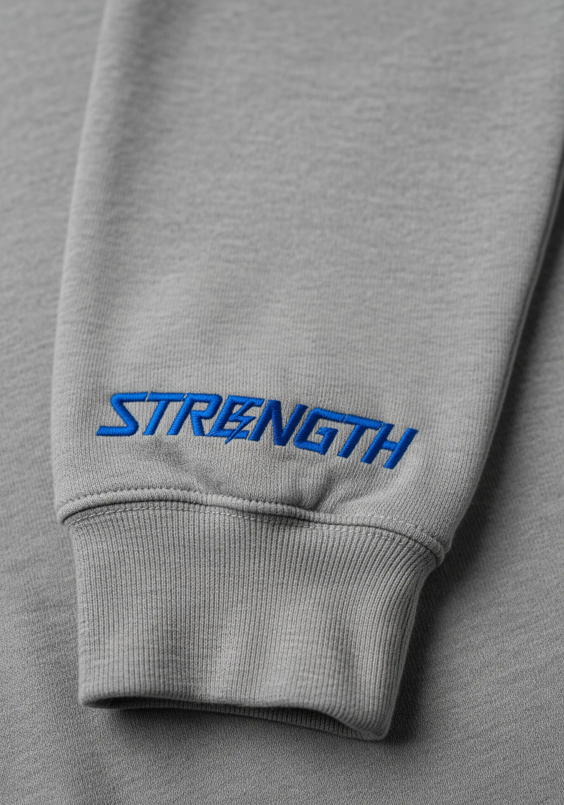 The word 'strength' embroidered in blue on the cuff of a grey sweatshirt
