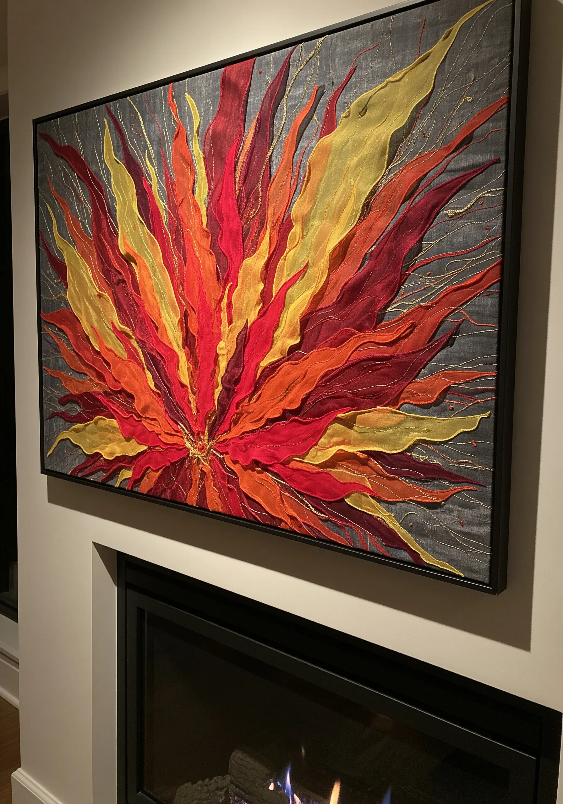 A large framed artwork of an abstract fire burst made with red, orange, and yellow sheer fabric strips.
