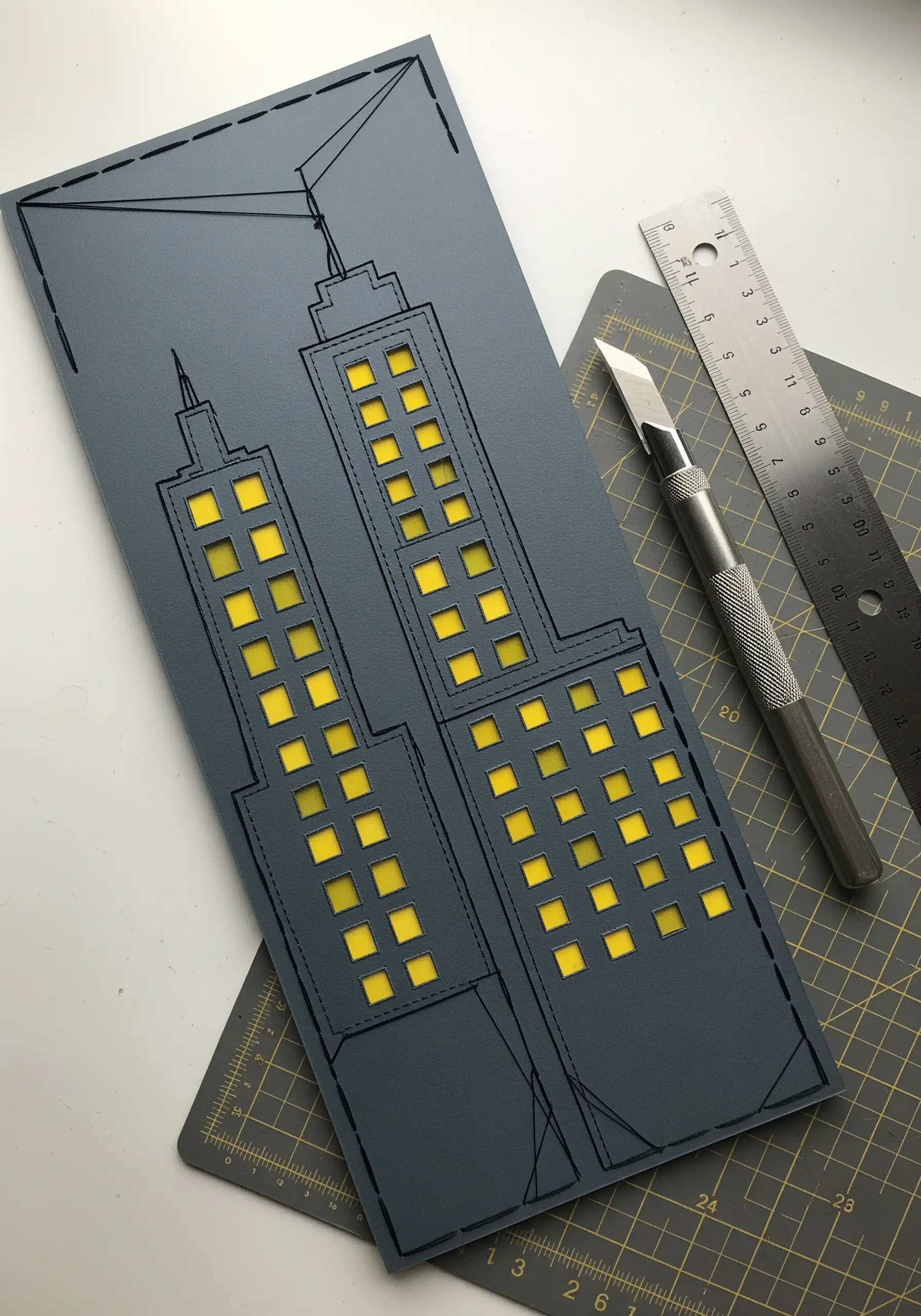 A paper-cut cityscape with black stitched outlines and glowing yellow paper windows.