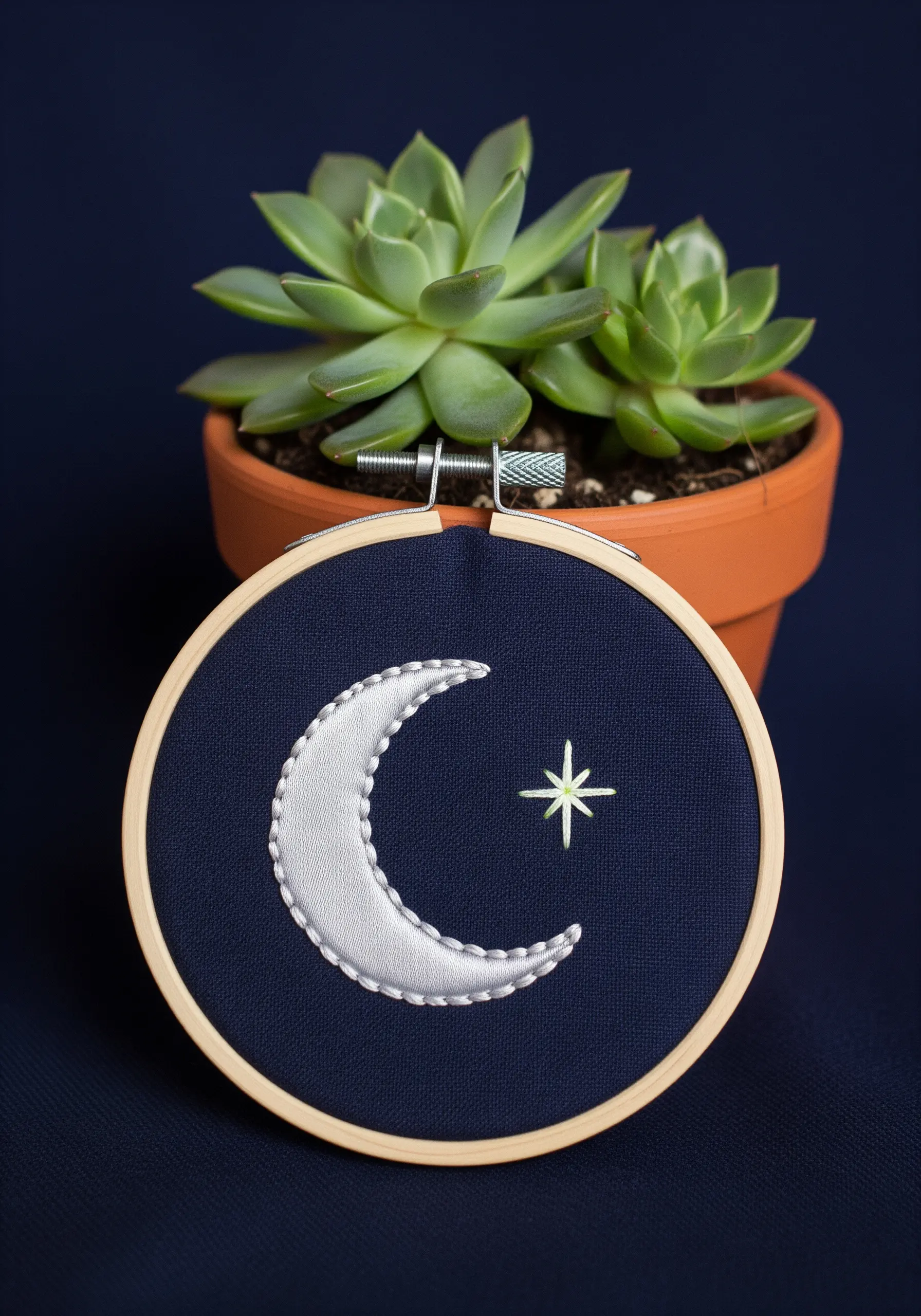 A satin-stitched crescent moon with a star on dark blue fabric.